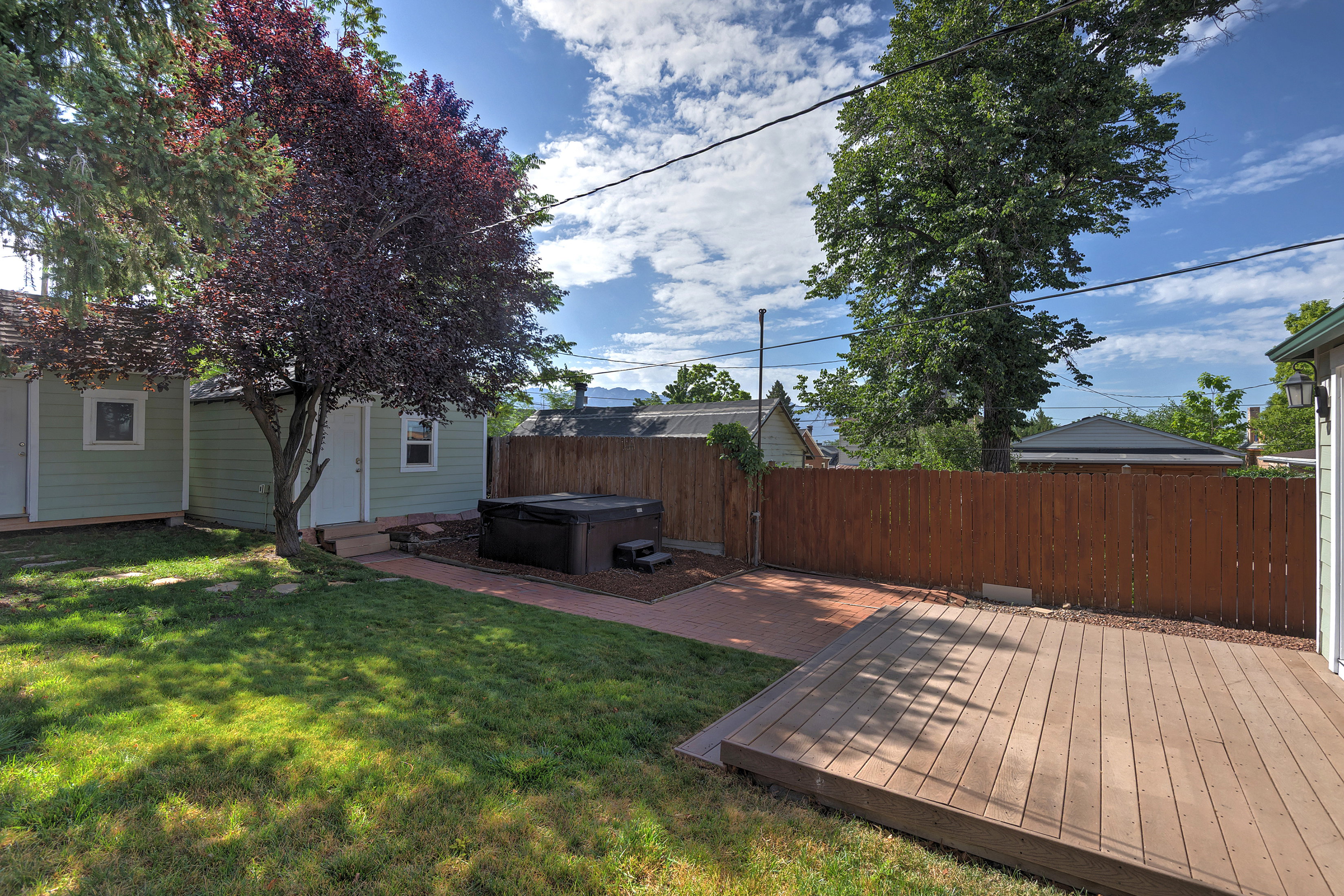 Expansive backyard featuring a wood-finish deck, brick paver patio, and mature landscaping