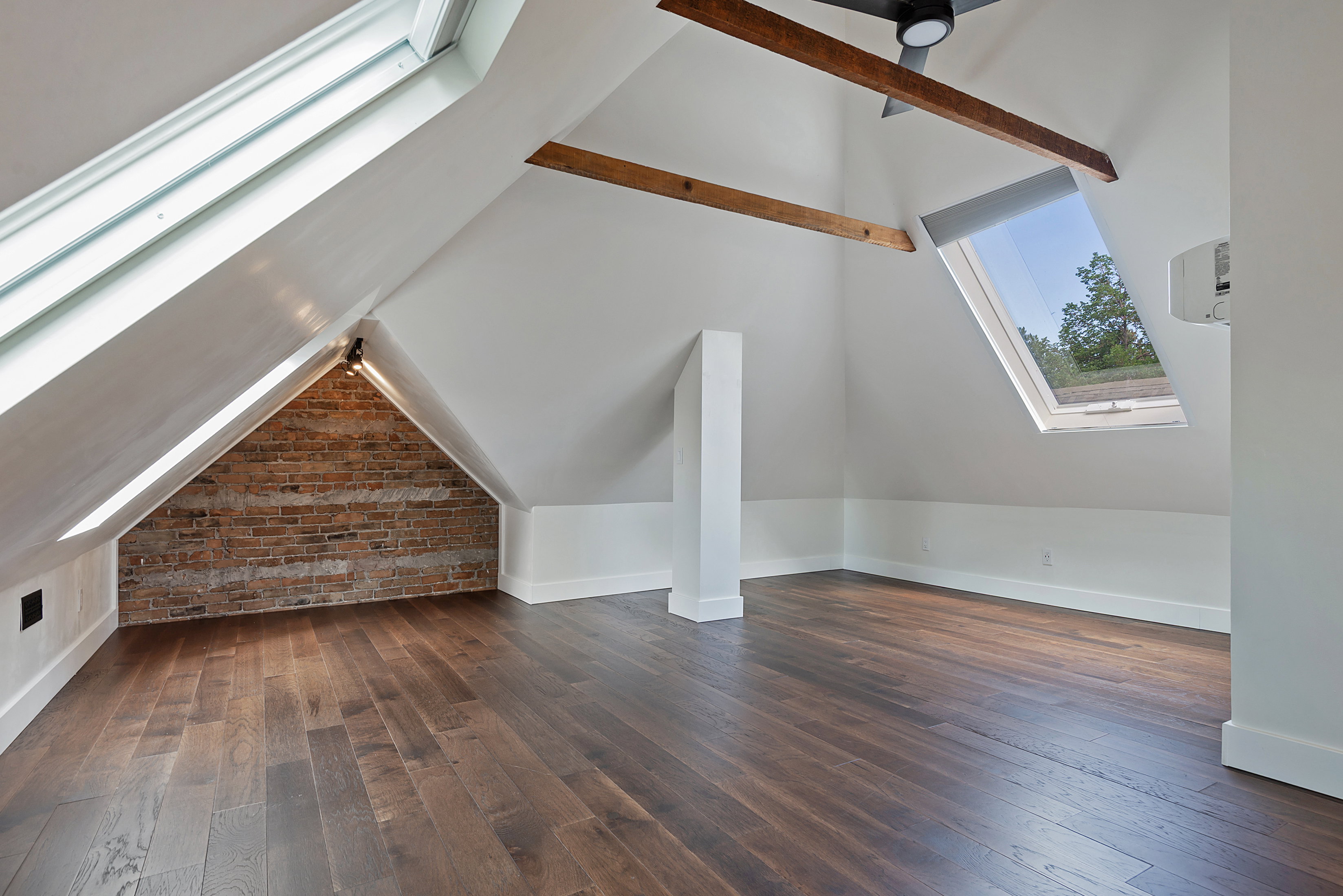 Spacious attic conversion with wood-finish flooring, exposed brick accent wall, and multiple skylights