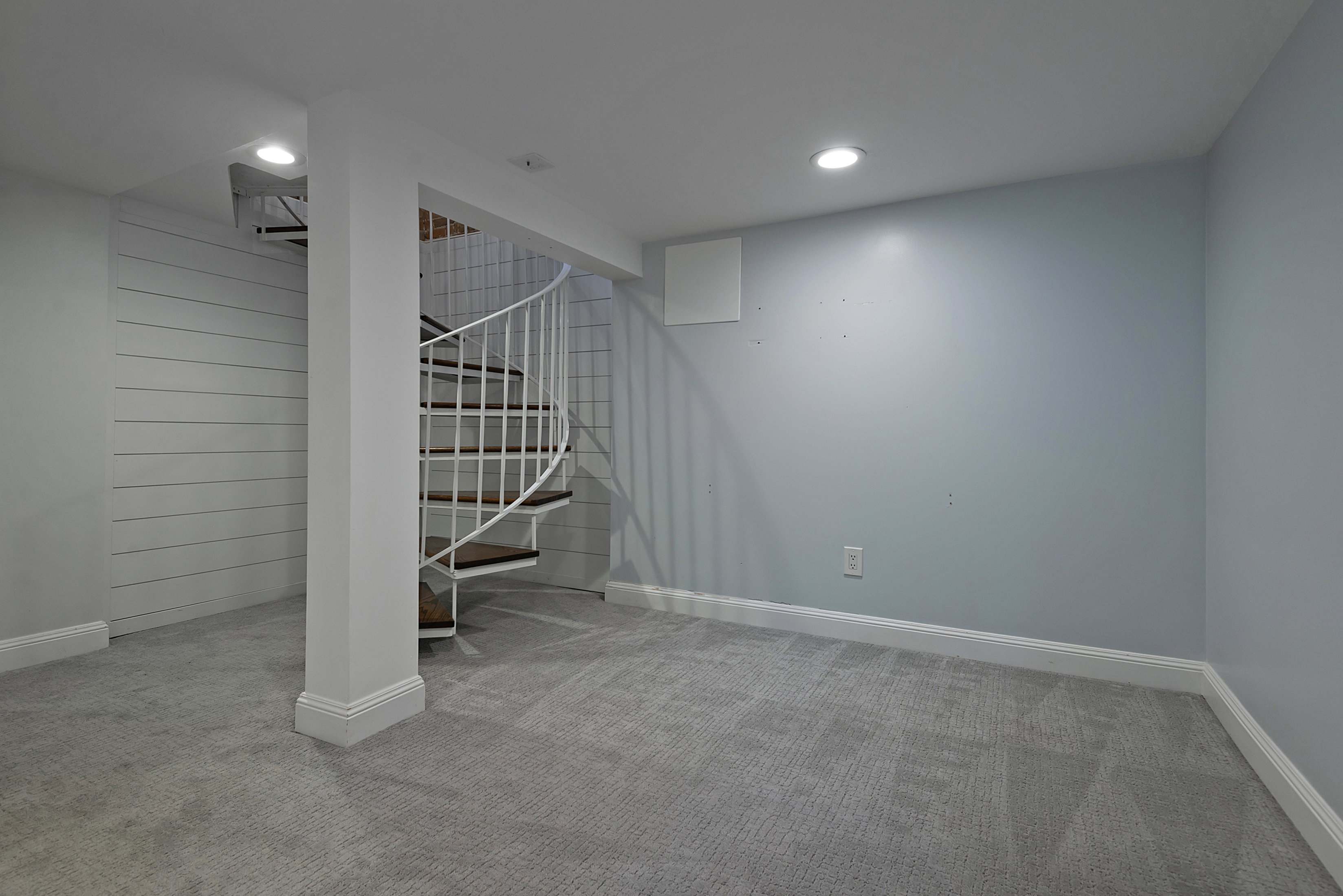 Spiral staircase with white railing and wood-finish treads, complemented by recessed lighting