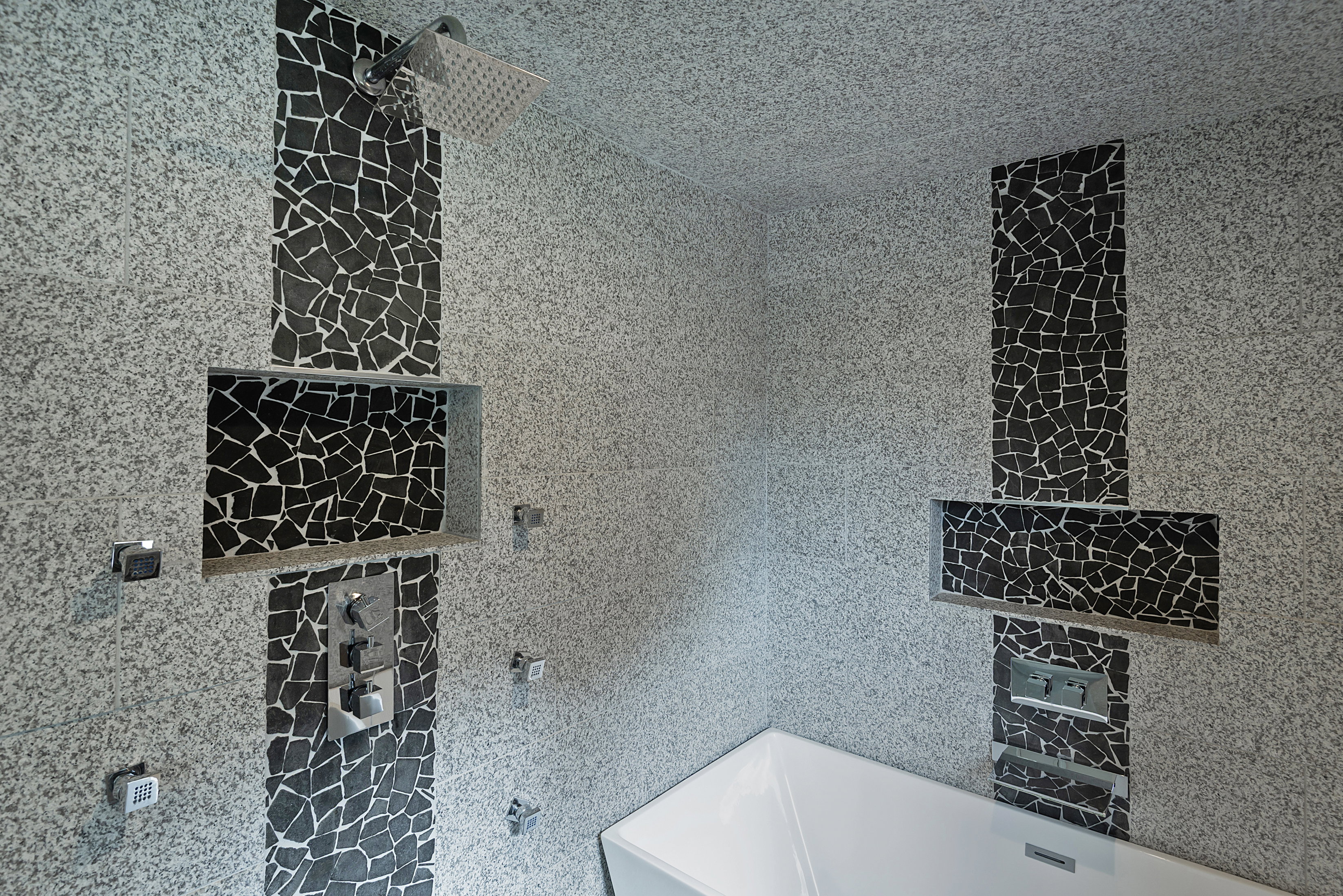 Contemporary shower and bathtub area featuring speckled gray wall tiling and accent bands of black mosaic tile
