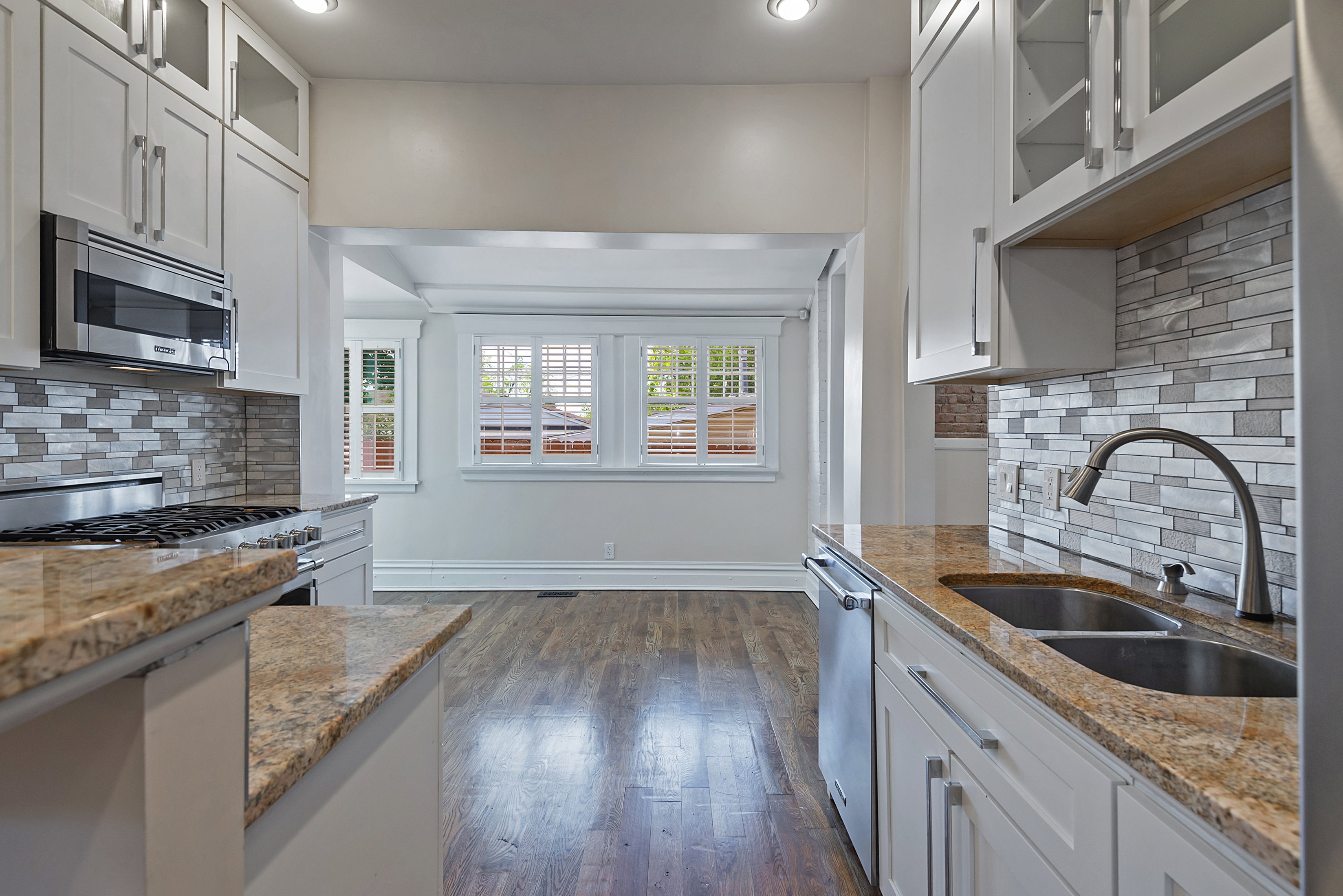 Kitchen featuring white cabinetry, granite countertops, stainless steel appliances, a tile backsplash, and dark wood-finish flooring