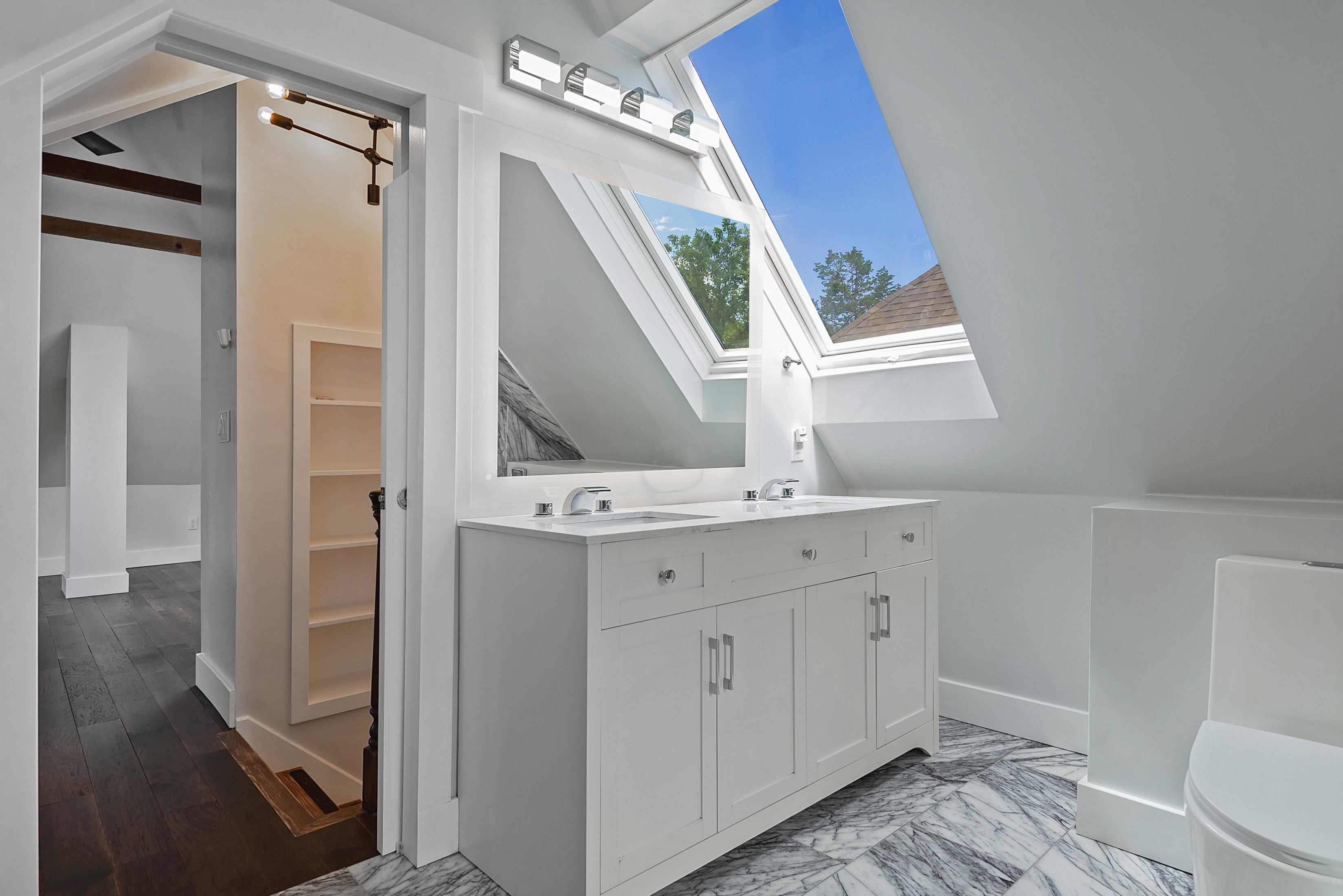Dual skylights illuminate this bathroom, featuring a double vanity with an integrated countertop, dual sinks, and under-cabinet storage