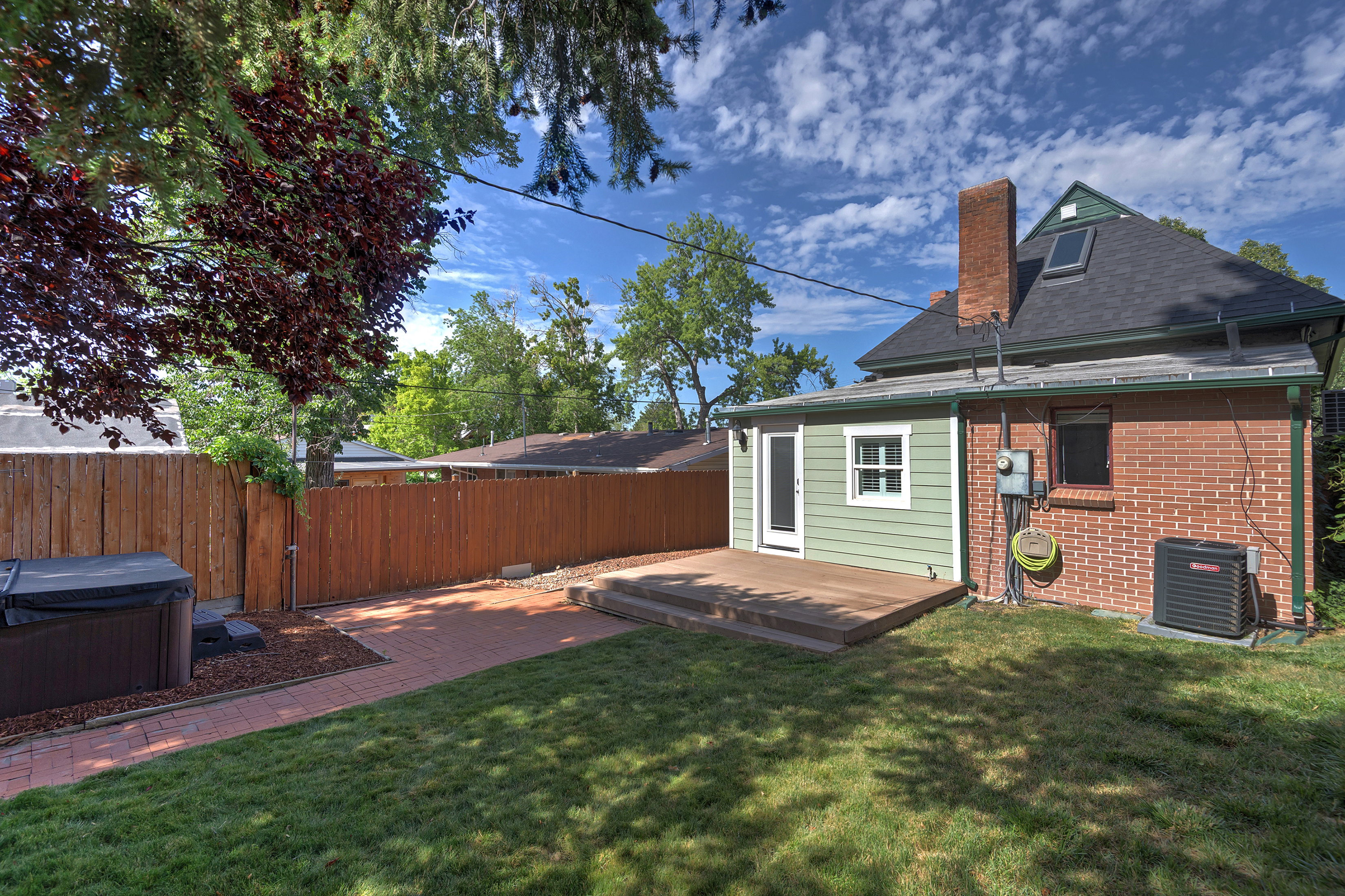 Expansive backyard featuring a manicured lawn, a raised wood-finish deck, and a brick pathway