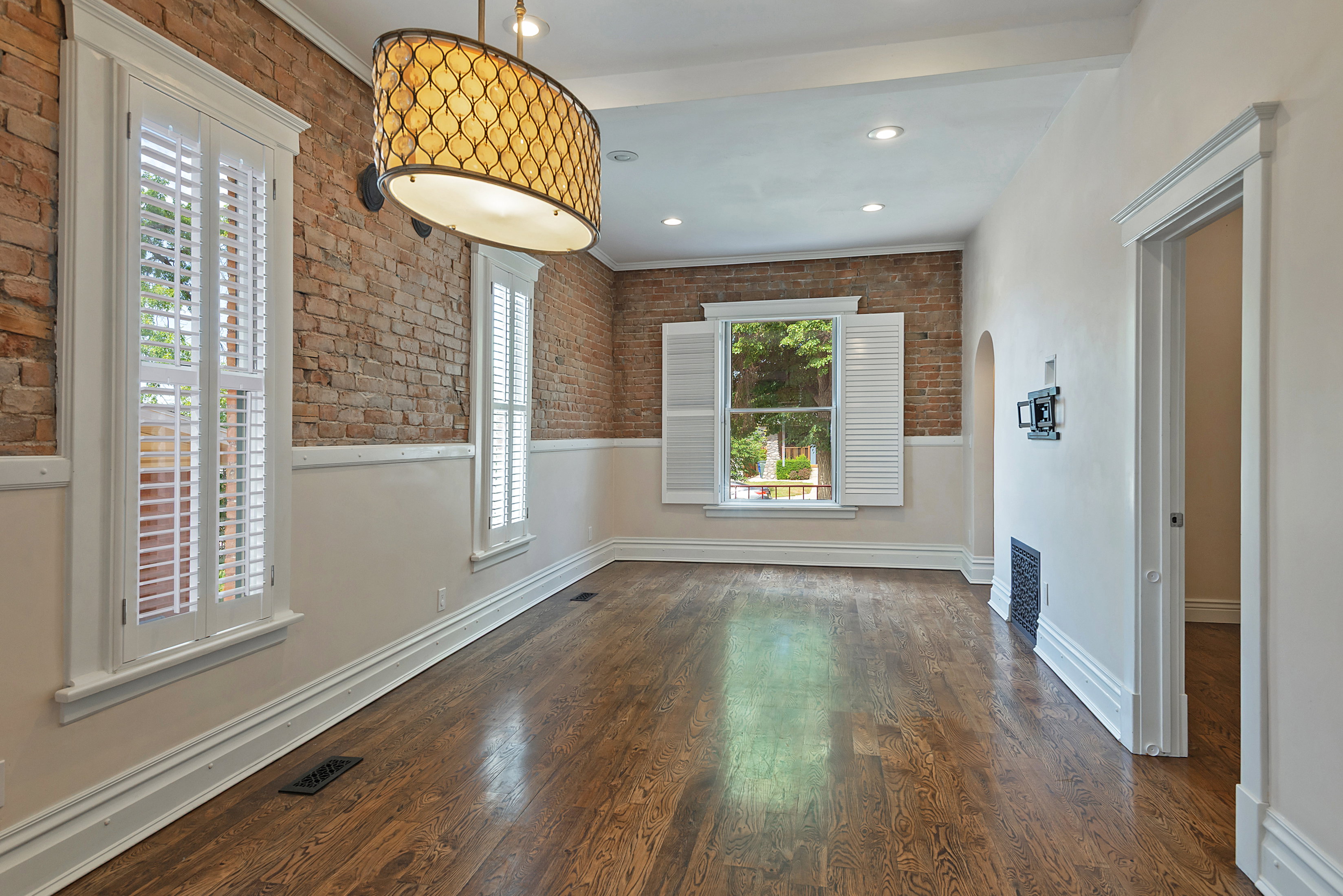 Room featuring exposed brick walls, wood-finish flooring, and white plantation shutters