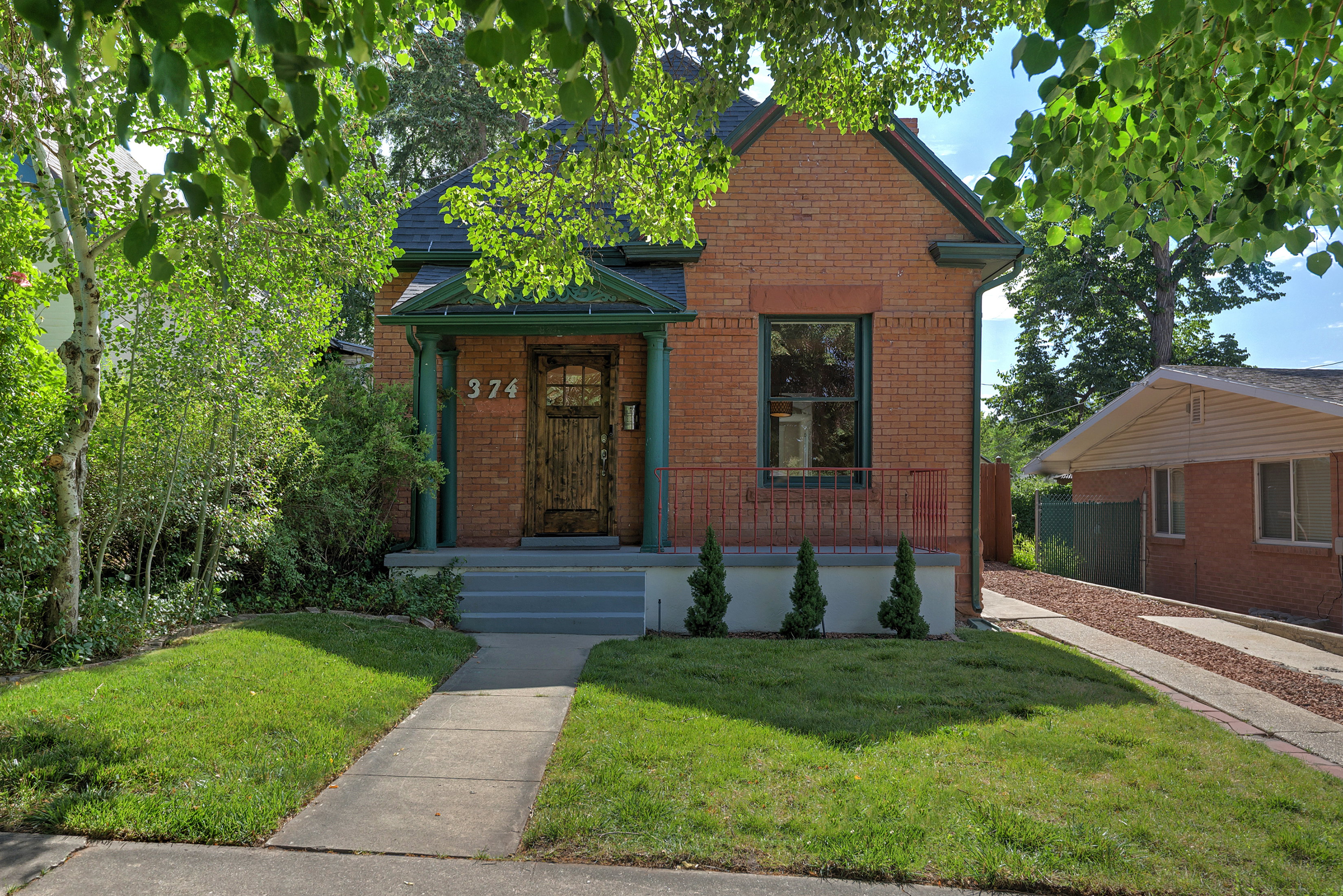 Brick exterior with a dark green trim, featuring a covered porch entry and a wood-paneled door