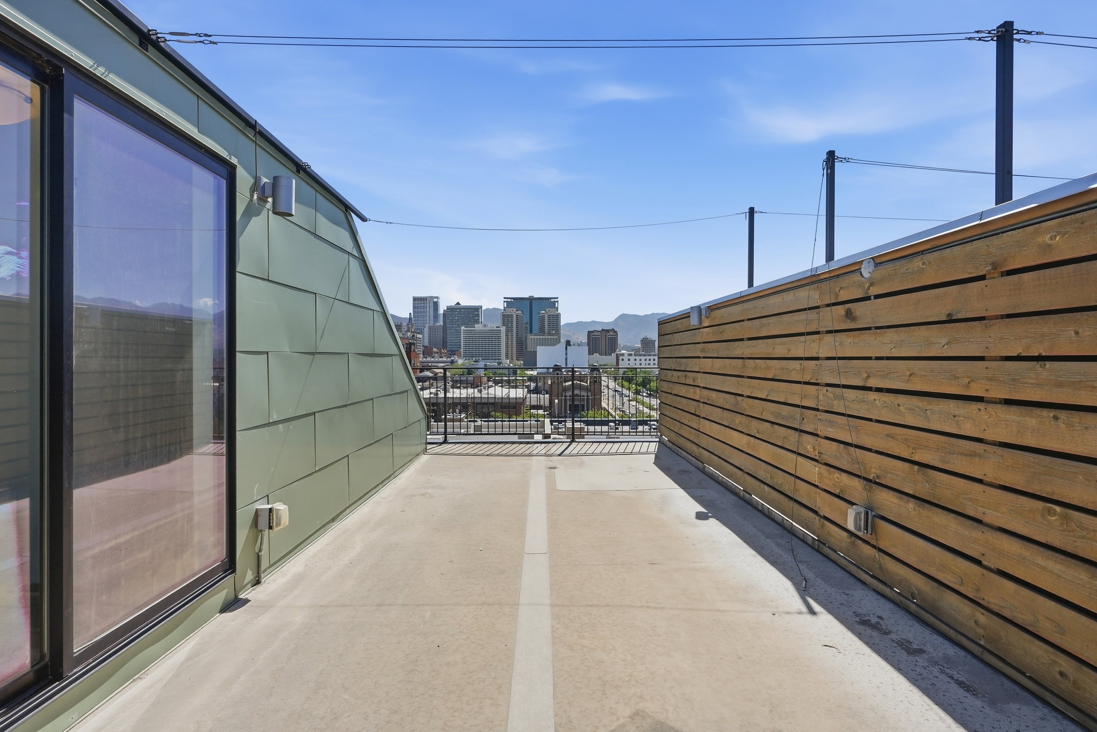 Rooftop deck featuring a concrete surface, green paneled siding, and a horizontal wood slat privacy wall