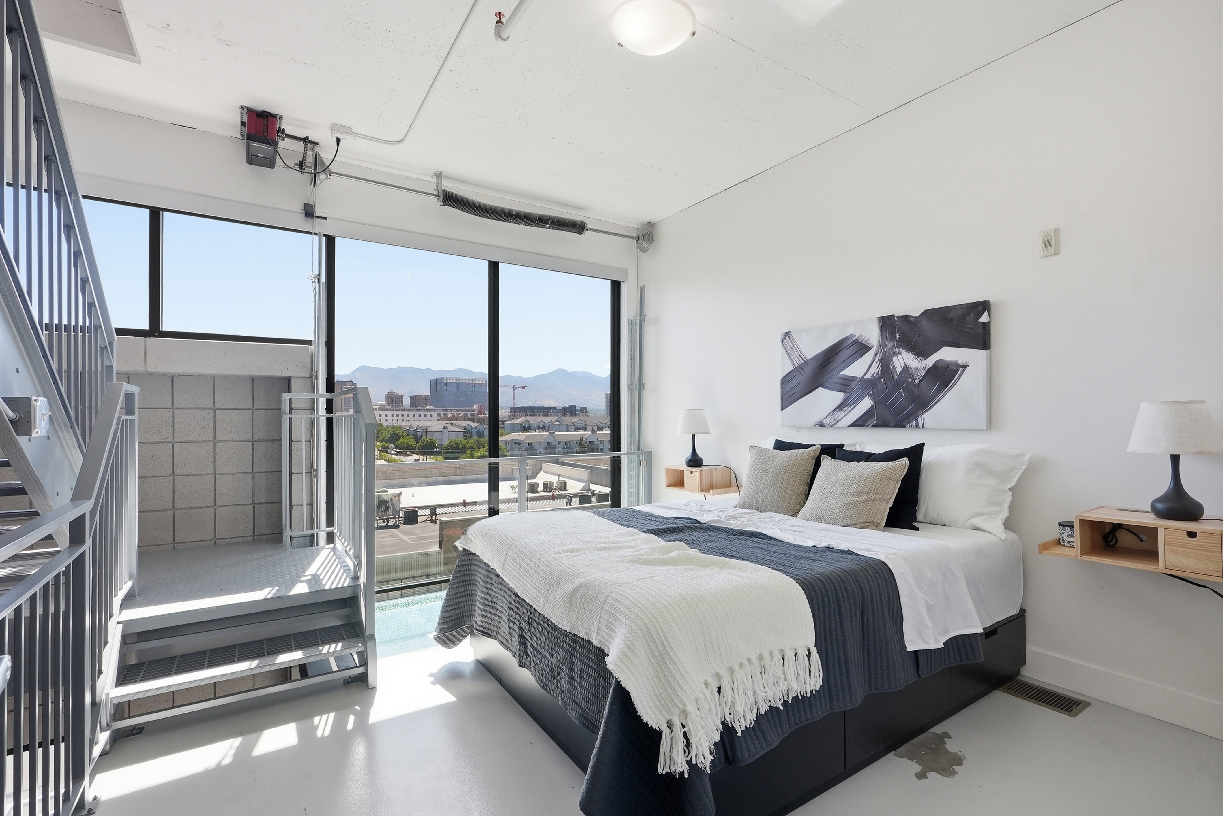 Expansive windows with mountain backdrop, industrial-style staircase and railing, white painted concrete flooring, recessed lighting, and high ceilings