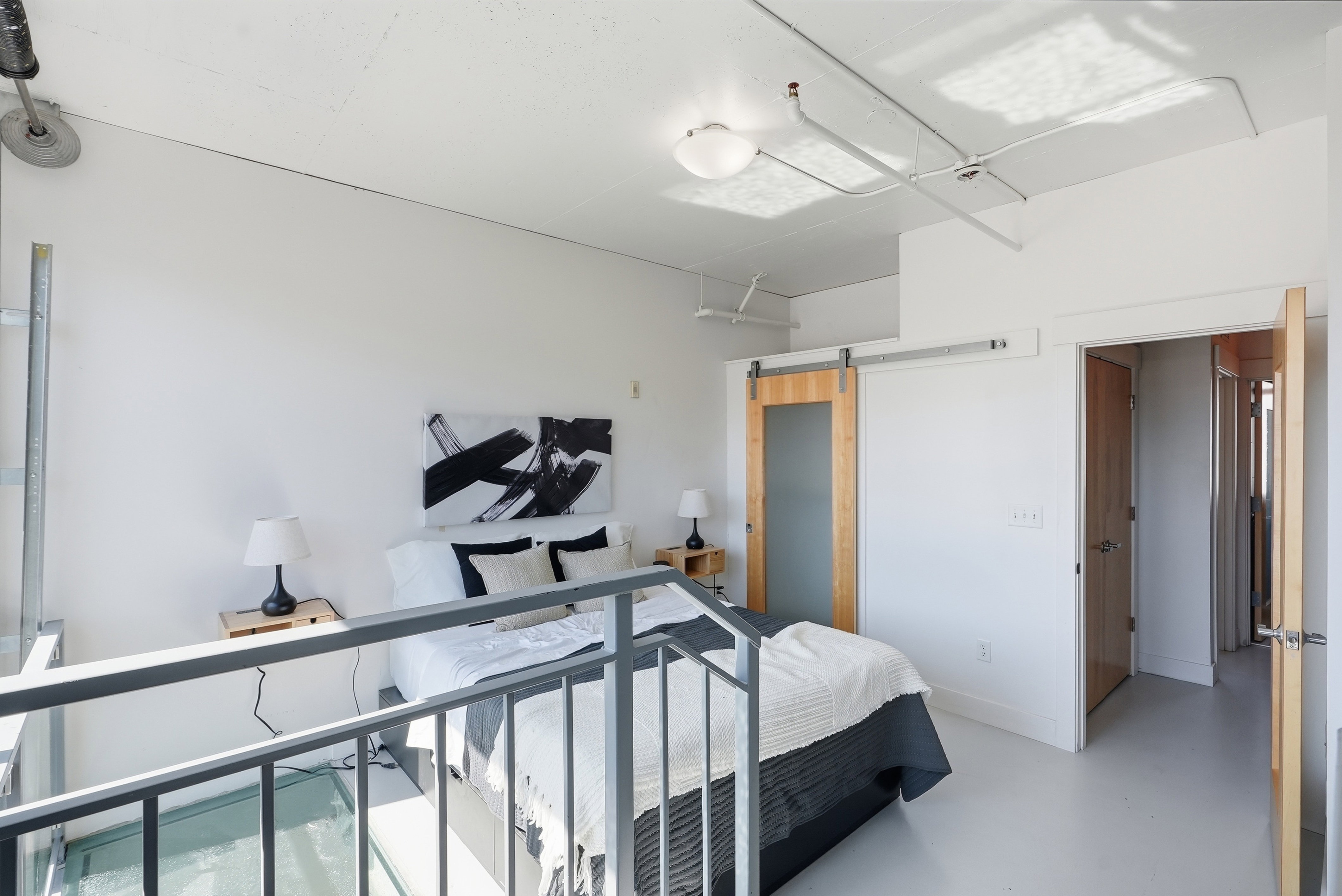 Loft bedroom featuring a barn door with frosted glass panel, exposed ceiling conduits, white walls, and light-toned flooring