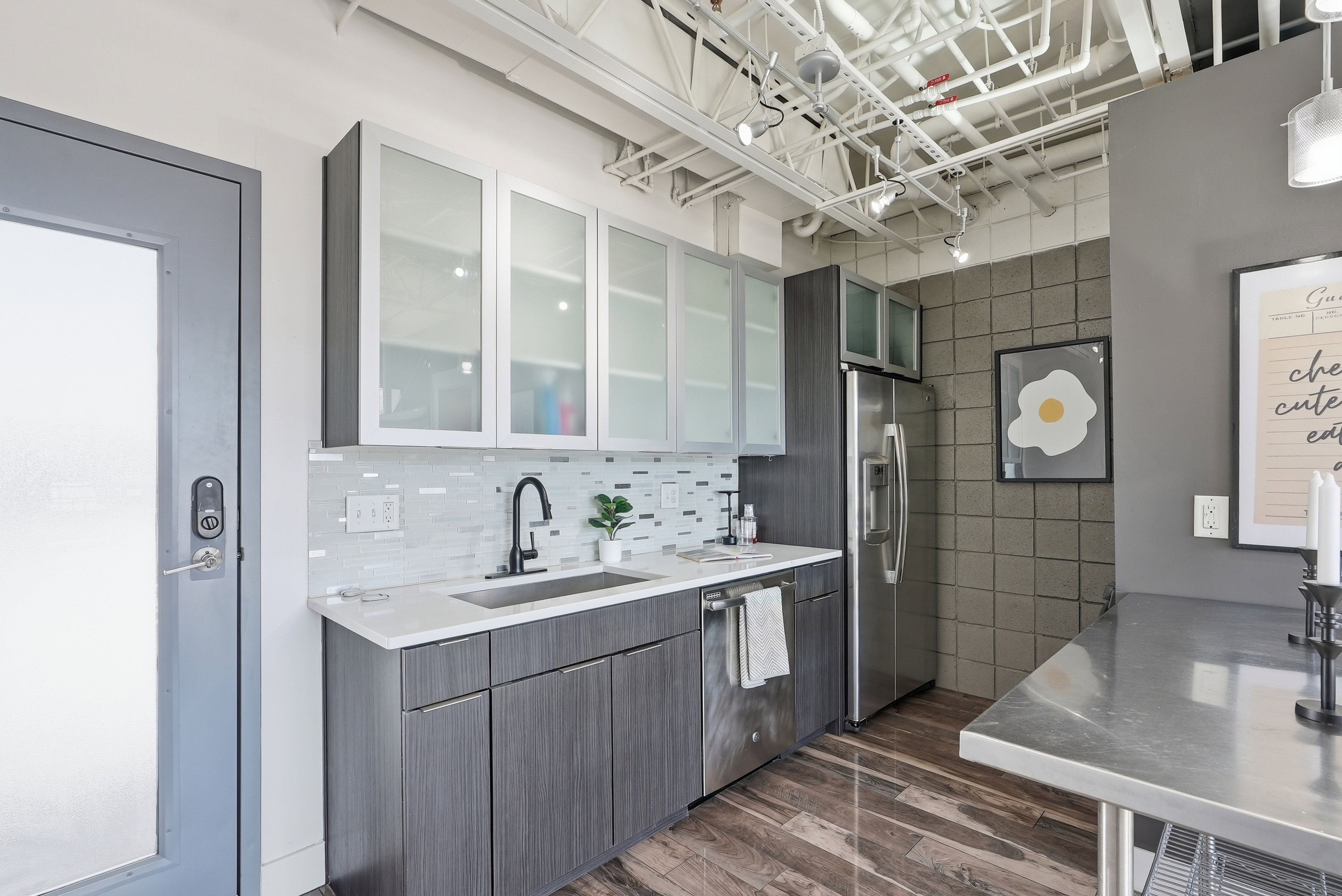 Contemporary kitchen featuring wood-finish flooring, white countertops, and a full suite of stainless steel appliances including a refrigerator and dishwasher