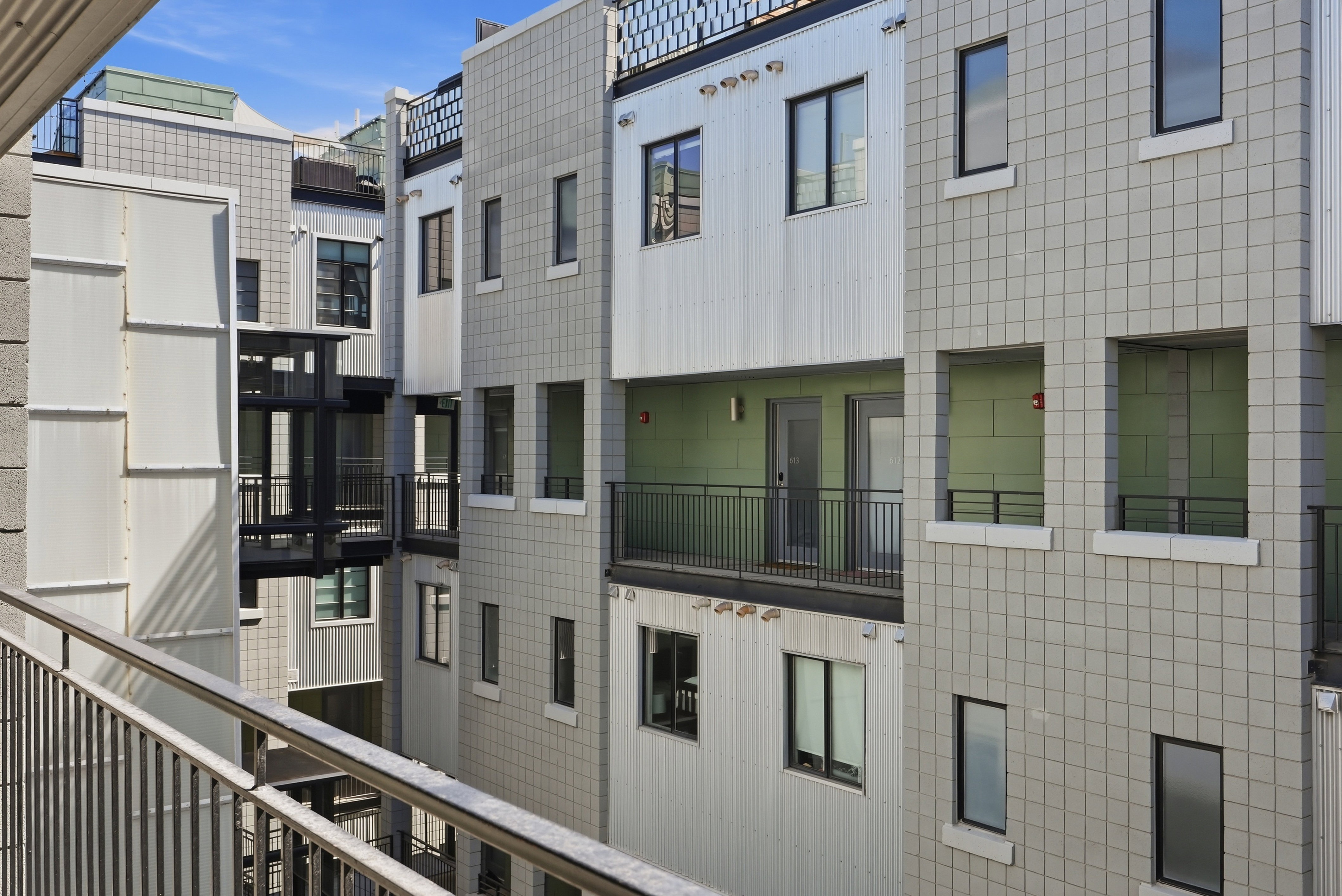 Modern multi-story building exterior featuring light grey block siding, white vertical paneling, and black-framed windows