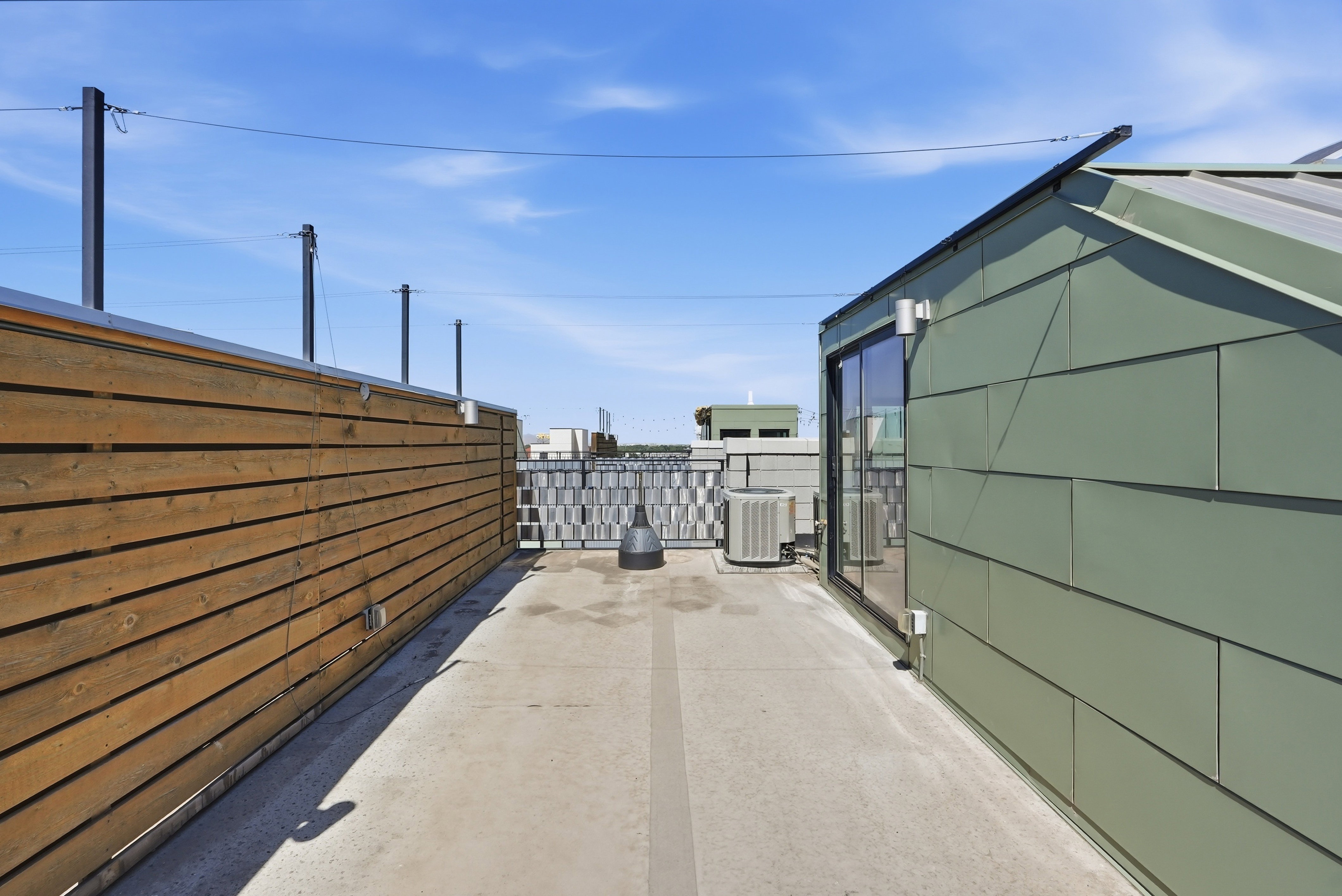 Rooftop deck featuring a concrete surface, a wood-slat privacy wall, and a green paneled structure with sliding glass doors