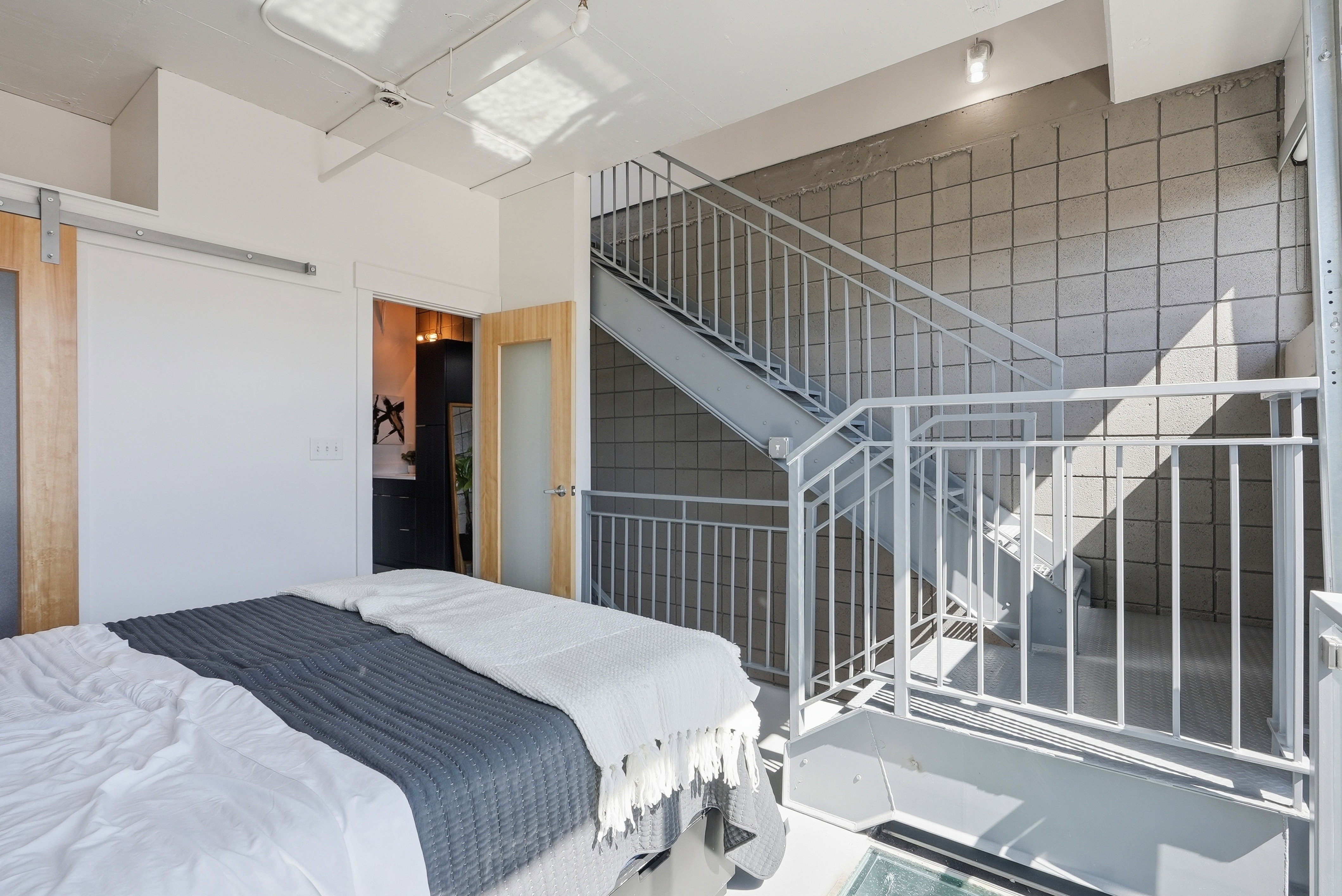 Exposed metal staircase with square grid wall detailing, light wood-finish barn door, and a frosted glass panel door