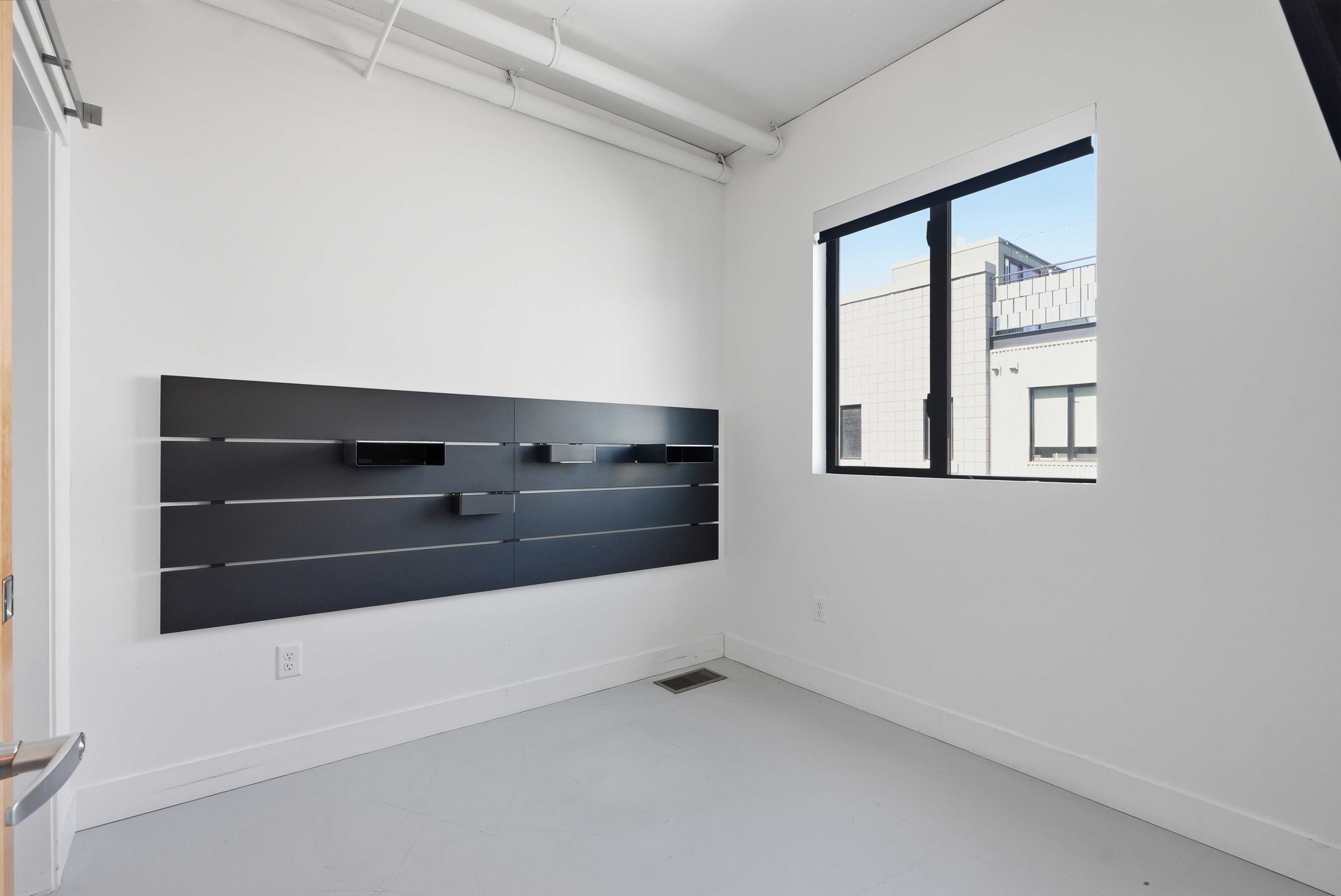 Room featuring a wall-mounted shelving unit, an exposed ceiling duct, and a window with black trim