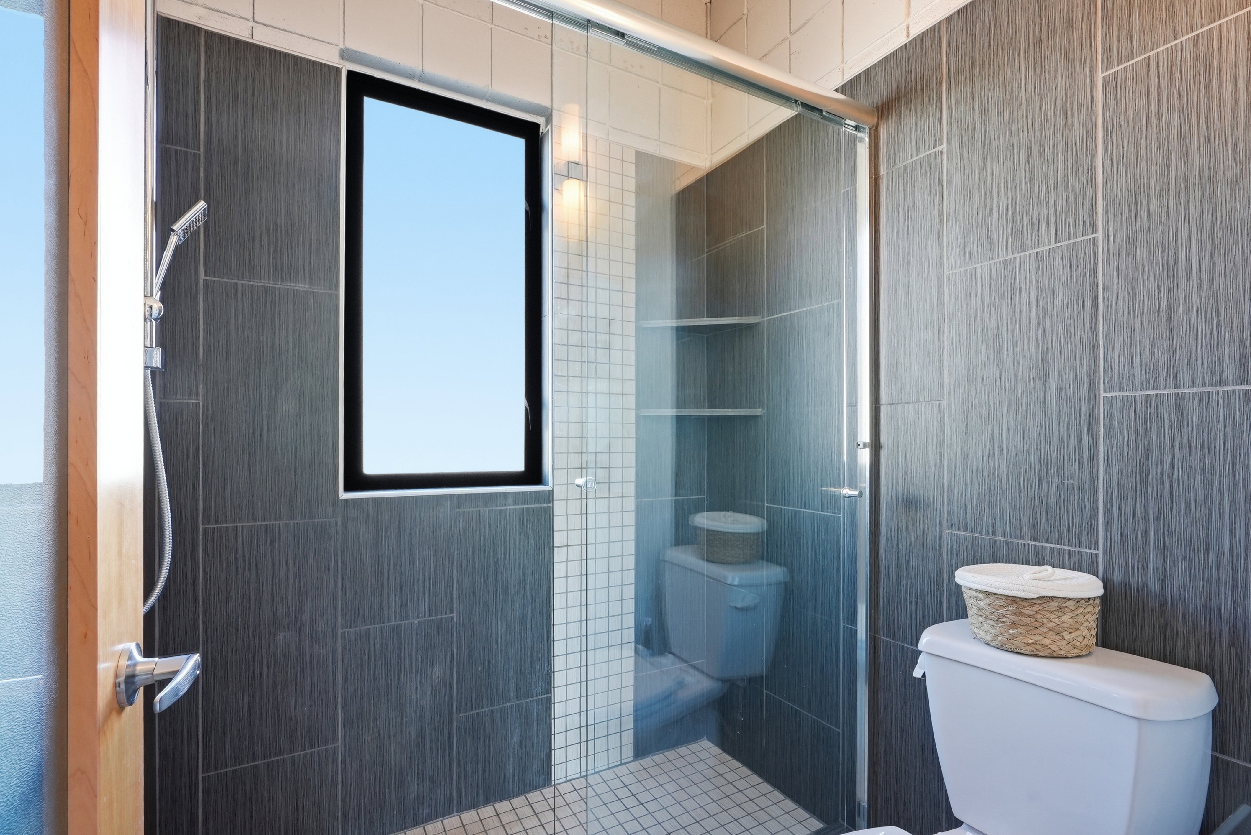 Contemporary bathroom featuring a walk-in shower with glass enclosure, dark gray textured wall tiling, and a window for natural light