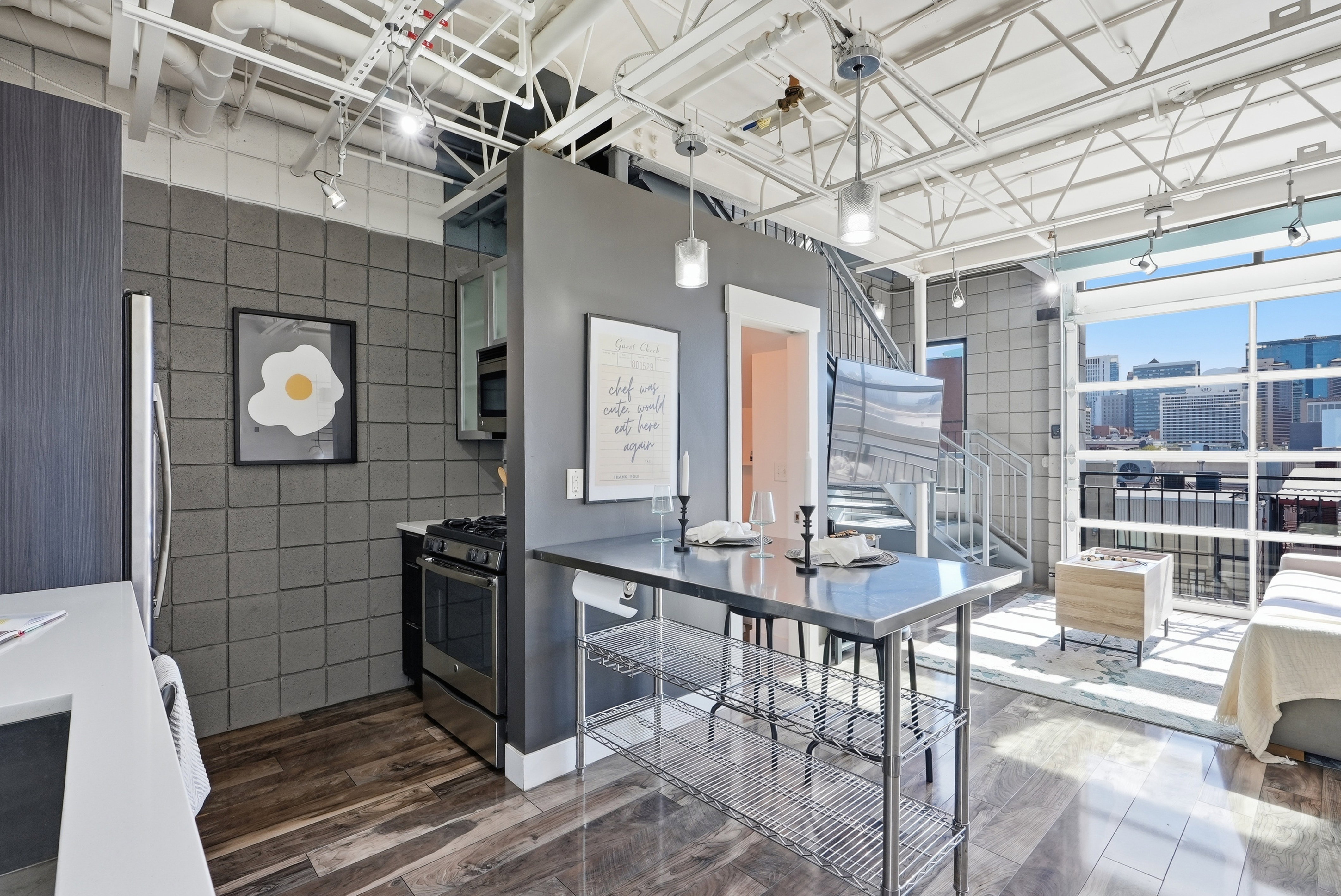 Open-concept living space featuring wood-finish flooring, exposed white ceiling trusses, and a full wall of industrial-style windows