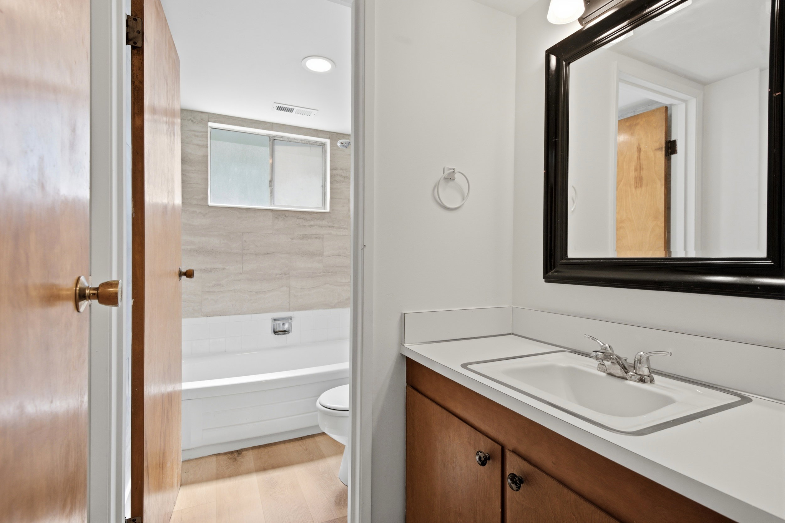 Bathroom featuring a wood-finish vanity with an integrated sink, white countertop, and a framed mirror