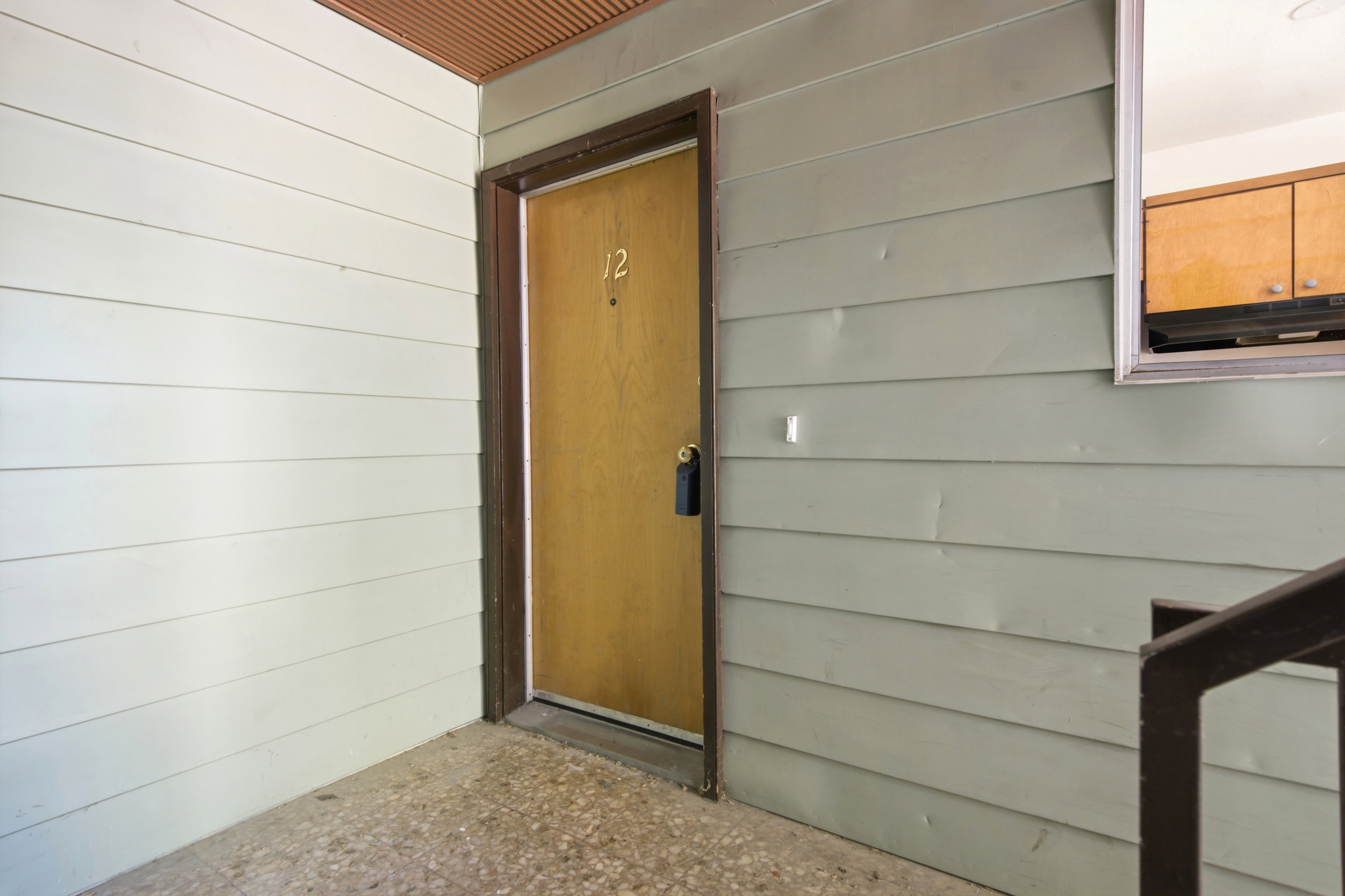 Entry door with brass house numbers, dark trim, and a black key lockbox