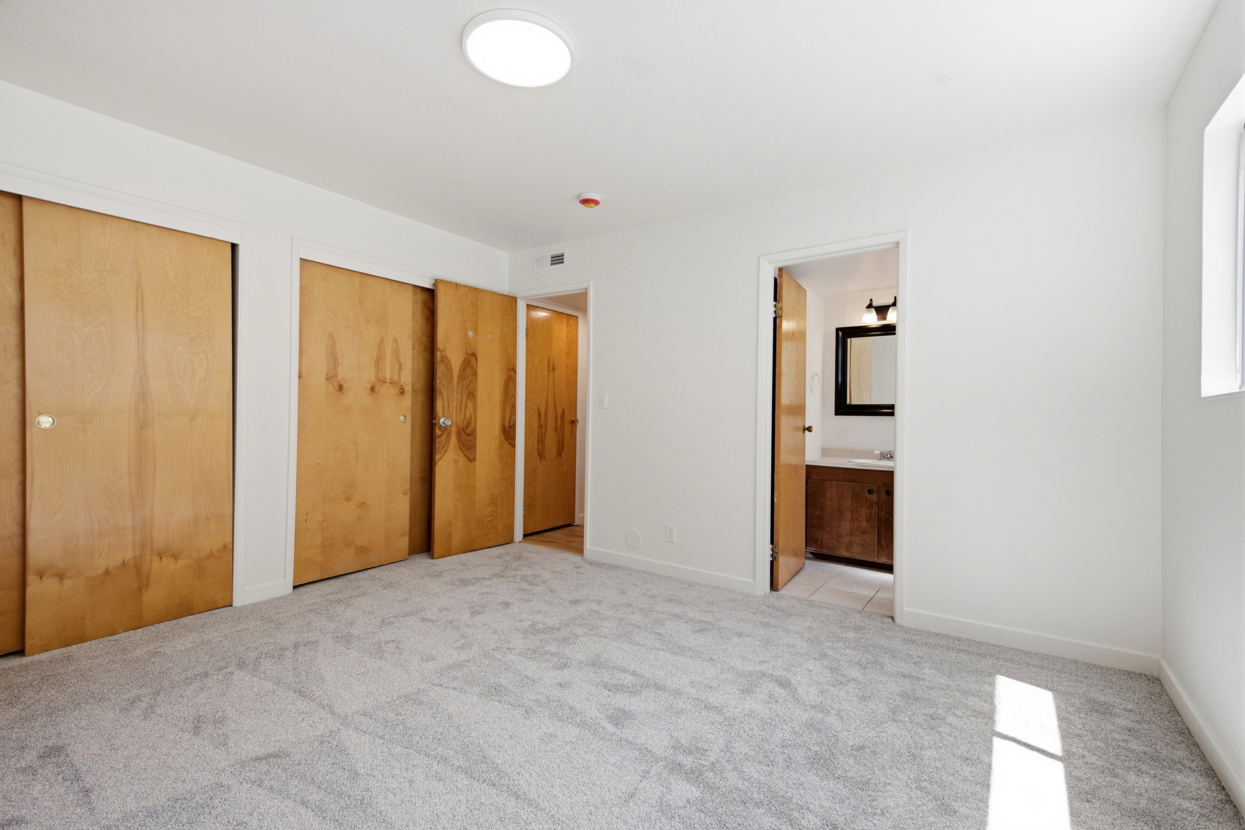 Carpeted room featuring multiple wood-finish sliding closet doors, a flush-mount ceiling light fixture, and a window for natural illumination