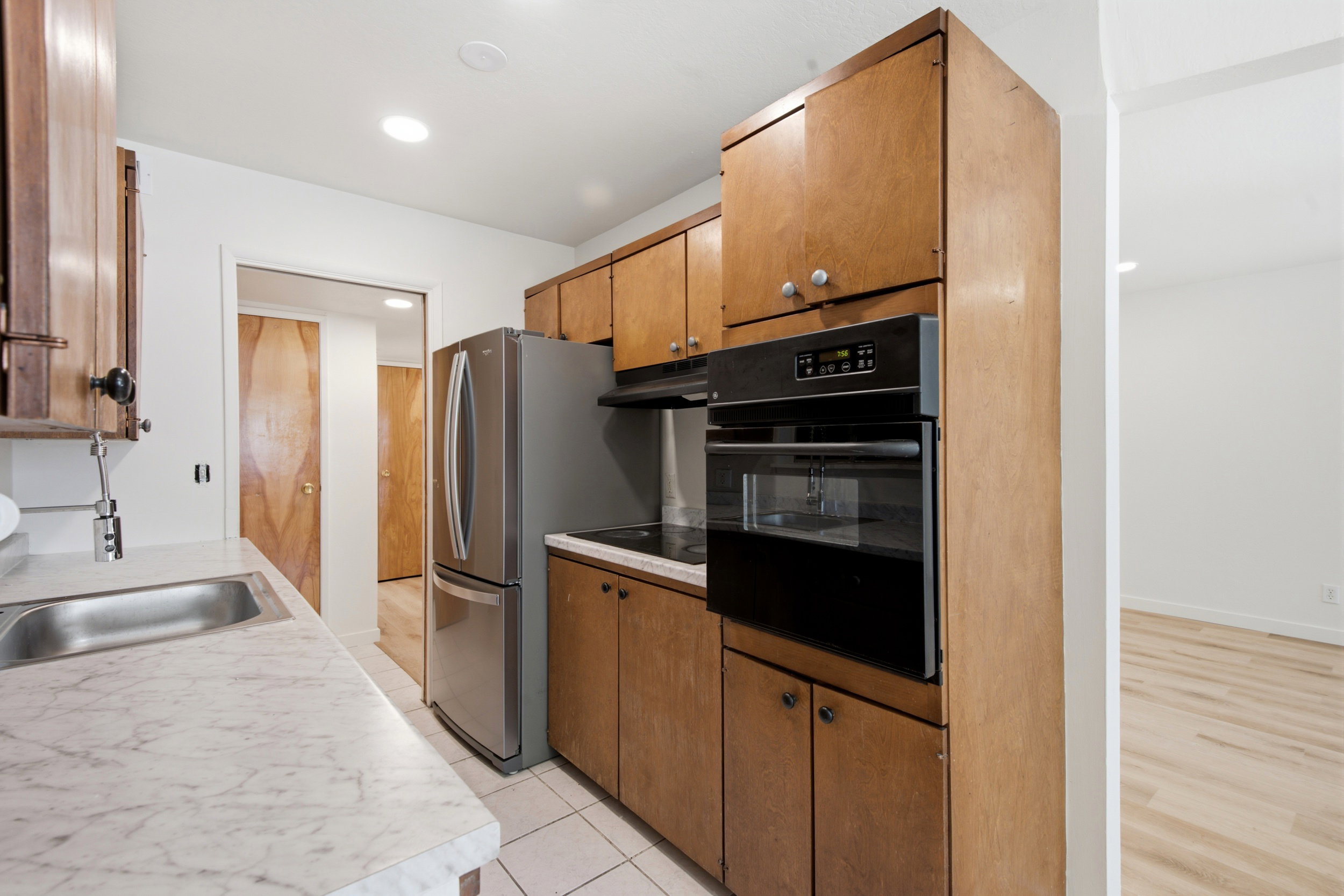 Kitchen featuring wood-finish cabinetry, stainless steel refrigerator, built-in oven, integrated cooktop, and light-toned countertop