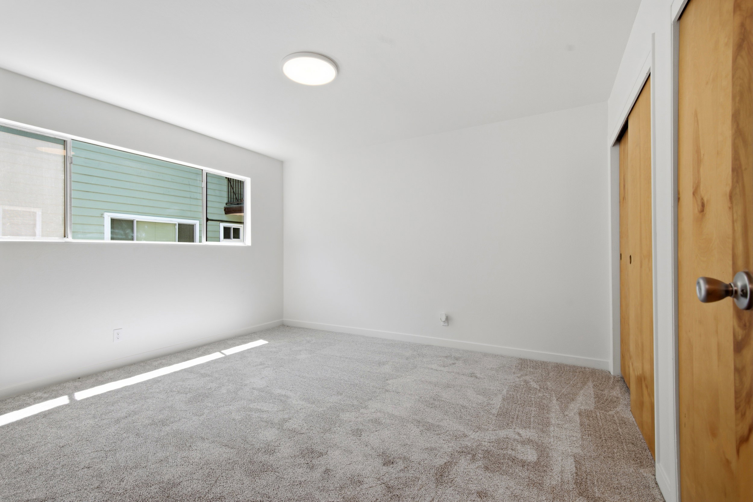 Carpeted room featuring a horizontal window, flush-mount ceiling light, and natural wood-finish closet doors with brushed nickel hardware