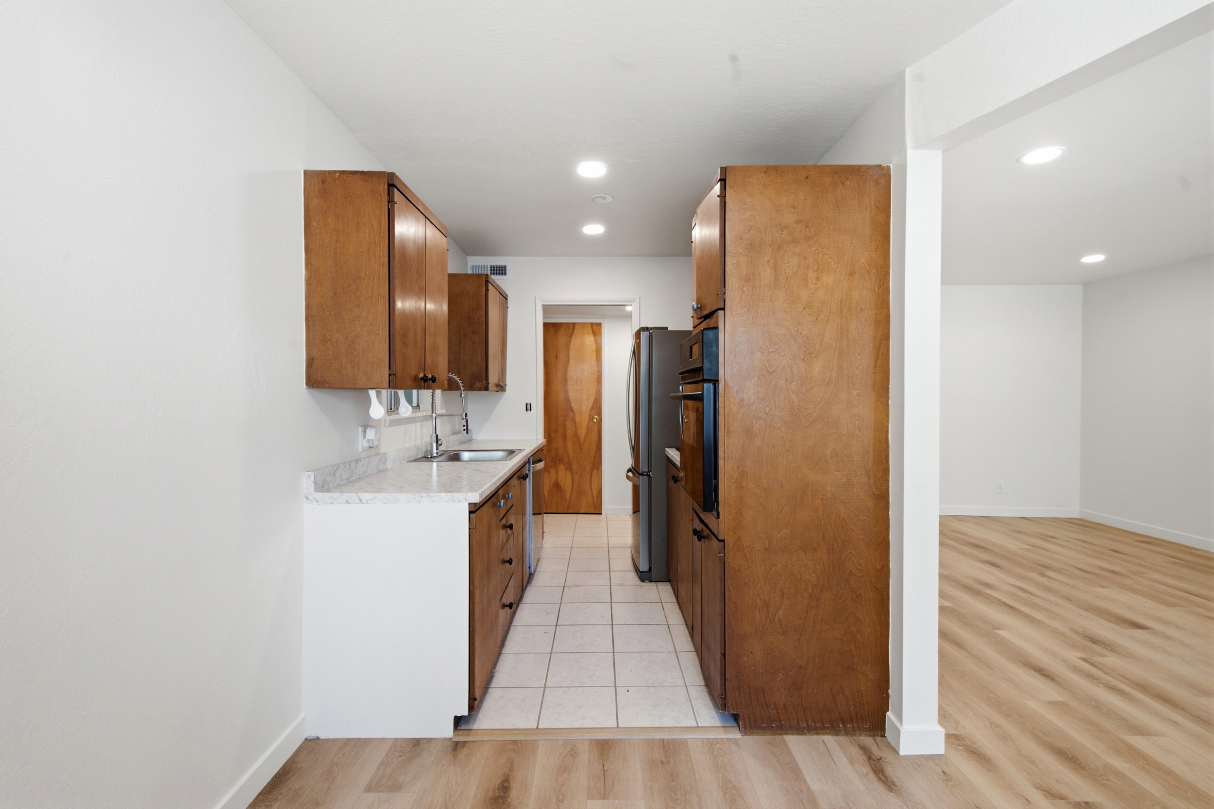 Galley kitchen featuring wood cabinetry, stone-look countertops, and a tile floor