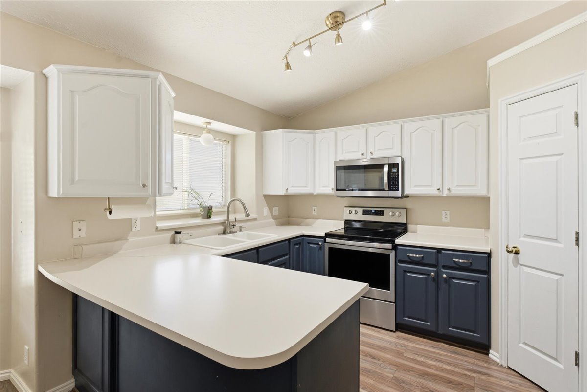 Kitchen featuring two-tone cabinetry, white countertops, stainless steel appliances, and wood-finish flooring