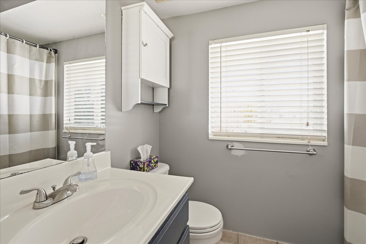 Bathroom featuring a single vanity with an integrated sink, brushed nickel faucet, wall-mounted mirror, and white wall cabinet with open shelving