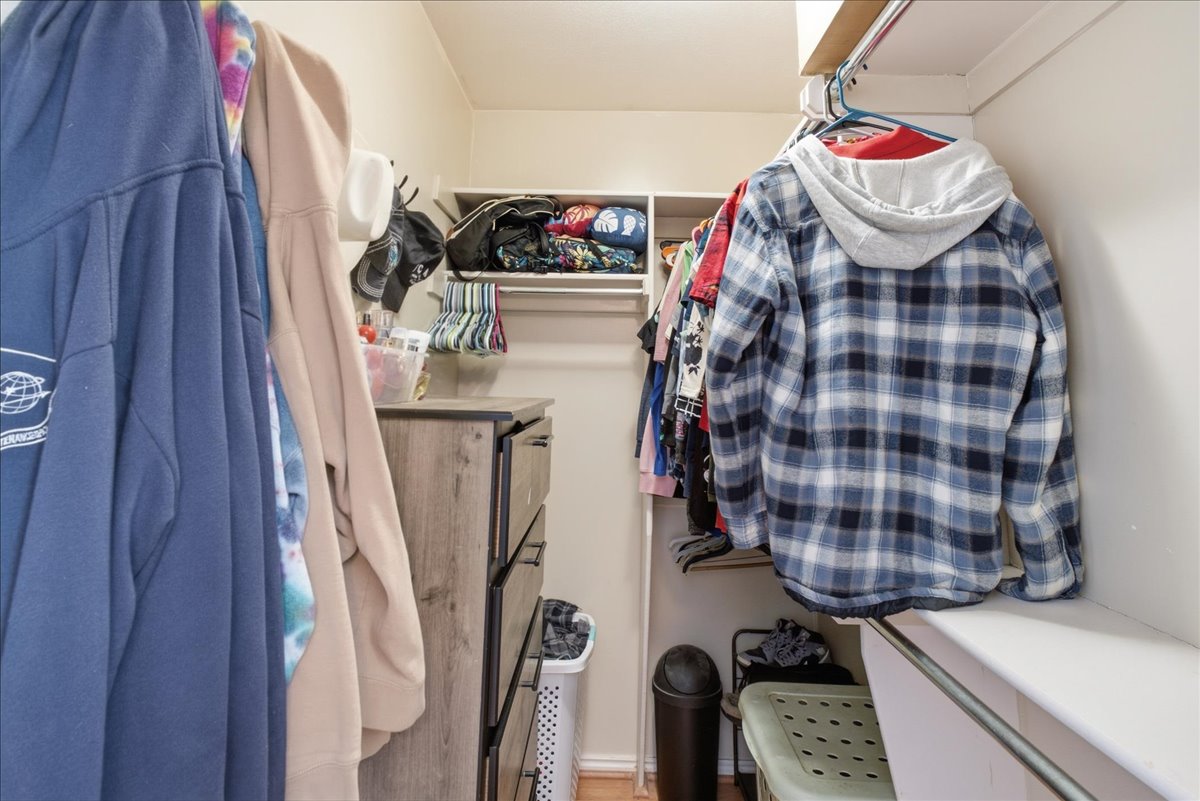 Walk-in closet featuring white shelving units, a built-in hanging rod, and a wood-finish dresser with dark hardware