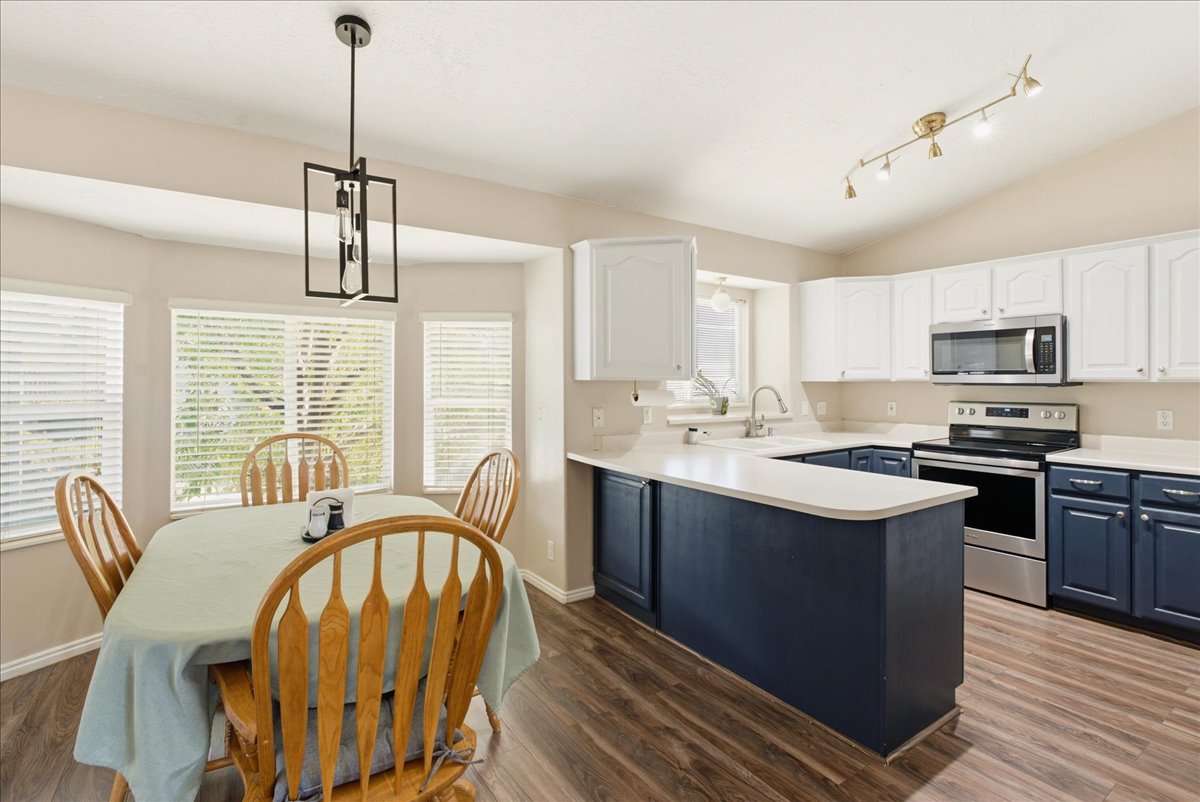 Kitchen featuring wood-finish flooring, two-tone cabinetry with white upper and navy lower units, stainless steel appliances, and light-toned countertops