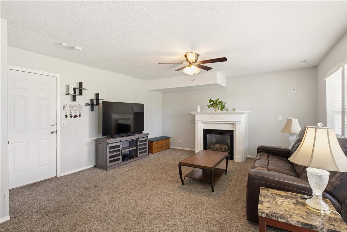Living room featuring a fireplace with a white mantel, ceiling fan, and carpeted flooring