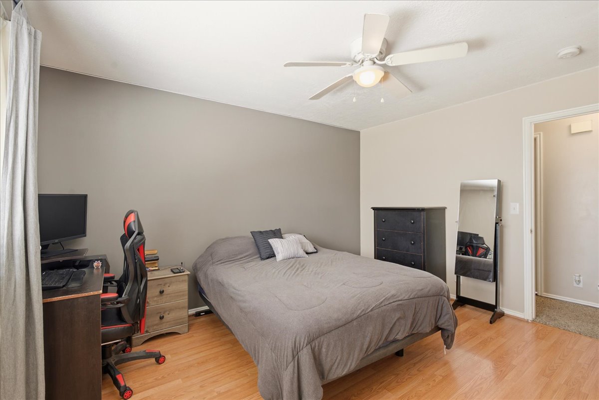 Bedroom featuring an accent wall, wood-finish flooring, a ceiling fan with integrated lighting, and direct access to an interior space