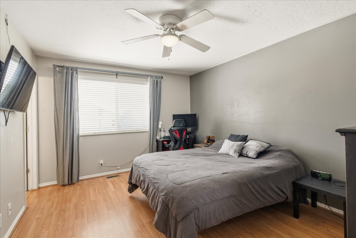 Bedroom featuring wood-finish flooring, a ceiling fan with integrated lighting, and a window with blinds and drapery