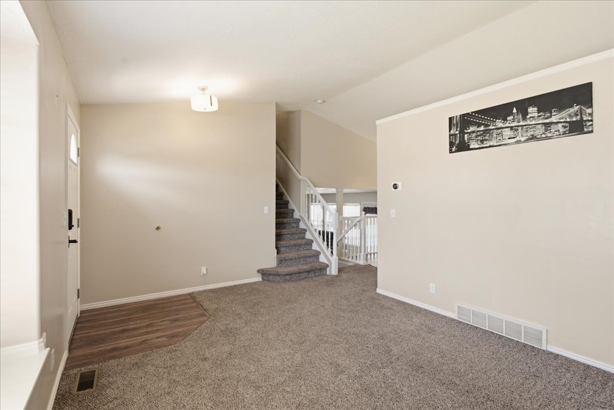 Entryway featuring a wood-finish flooring transition to carpet, staircase with white railing, and a vaulted ceiling