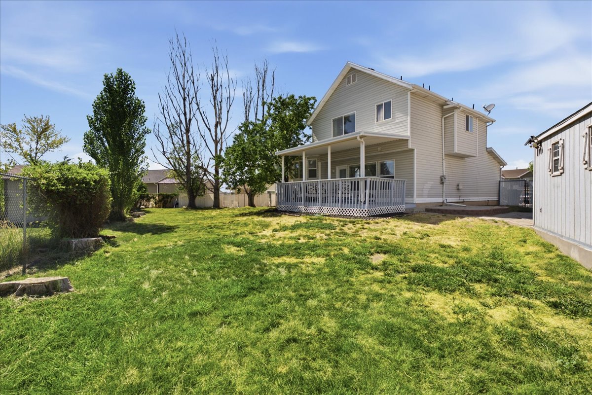 Expansive backyard featuring a covered deck, substantial lawn area, mature trees, and a detached storage shed