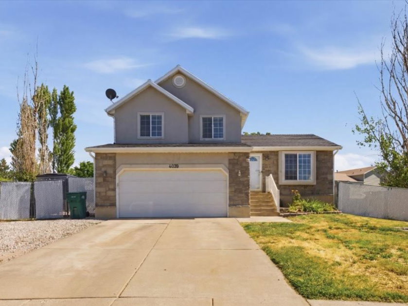 Two-story residence featuring a front entry with steps, an attached garage, a paved driveway, and a chain-link fence