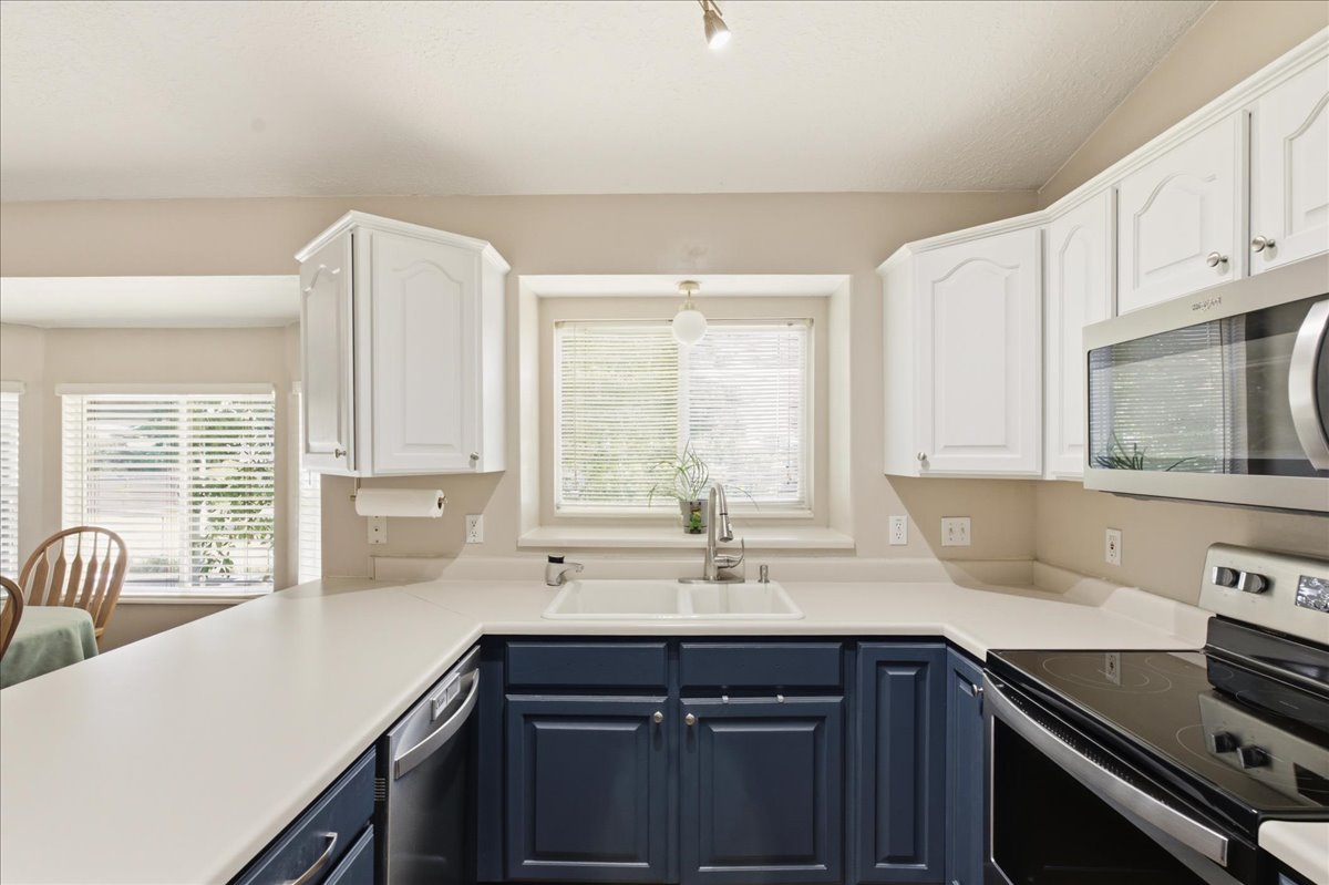U-shaped kitchen featuring two-tone cabinetry, a double basin sink with a gooseneck faucet, light-toned countertops, and stainless steel appliances