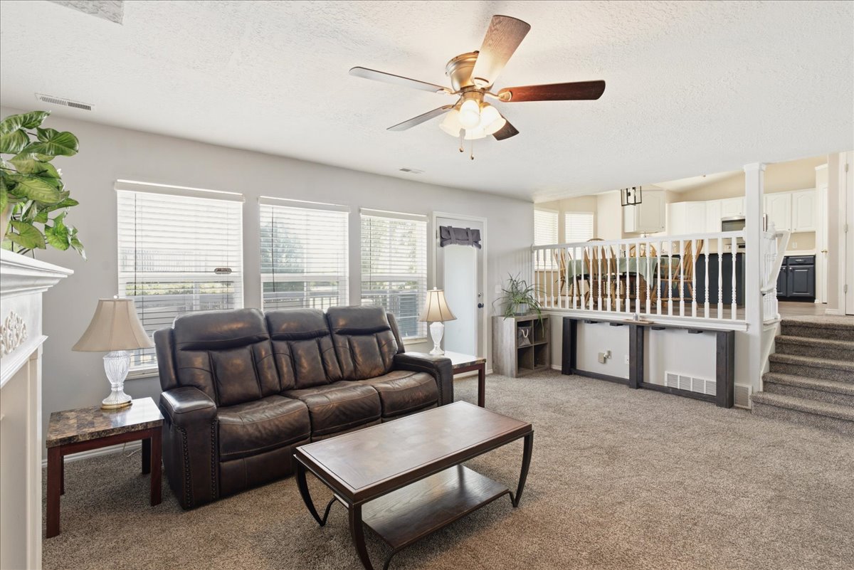 Carpeted living area featuring multiple windows with blinds, a ceiling fan with light fixture, and a decorative fireplace surround