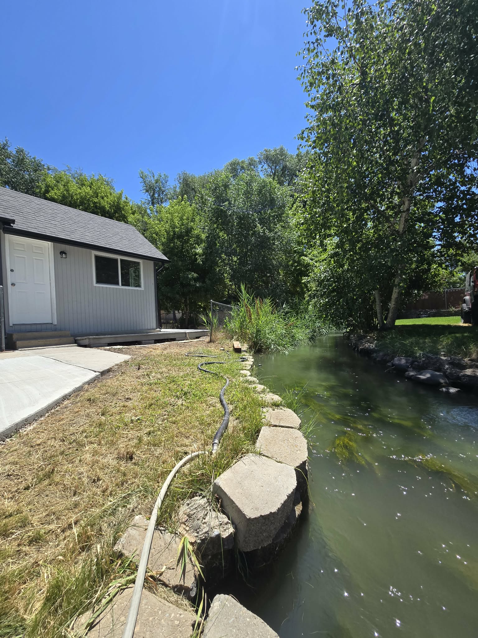 Waterfront property featuring a newly constructed exterior with siding, a dark shingle roof, and a concrete patio