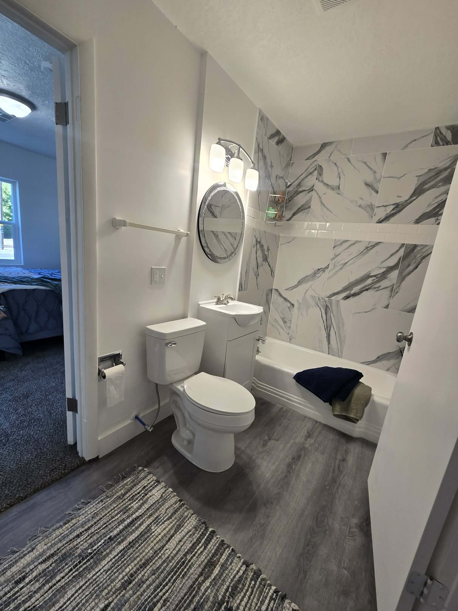 Bathroom with wood-finish flooring, a white vanity with an integrated sink, a white toilet, and a white bathtub