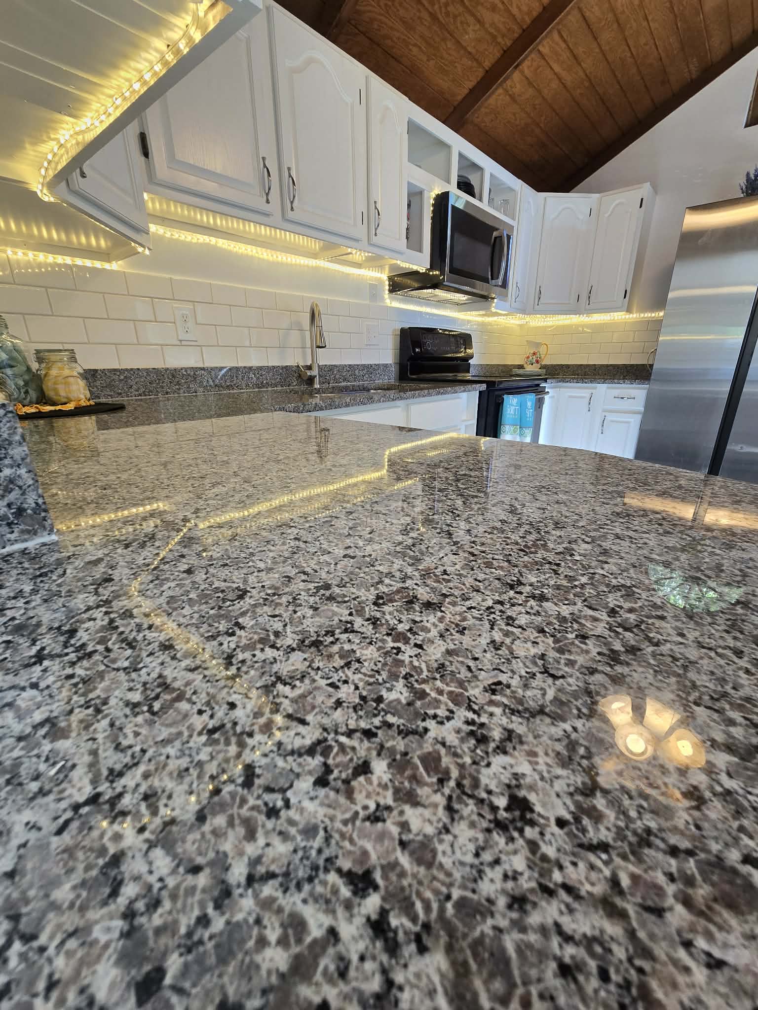 Kitchen featuring speckled countertops, white subway tile backsplash, white cabinetry with dark hardware, and a built-in microwave