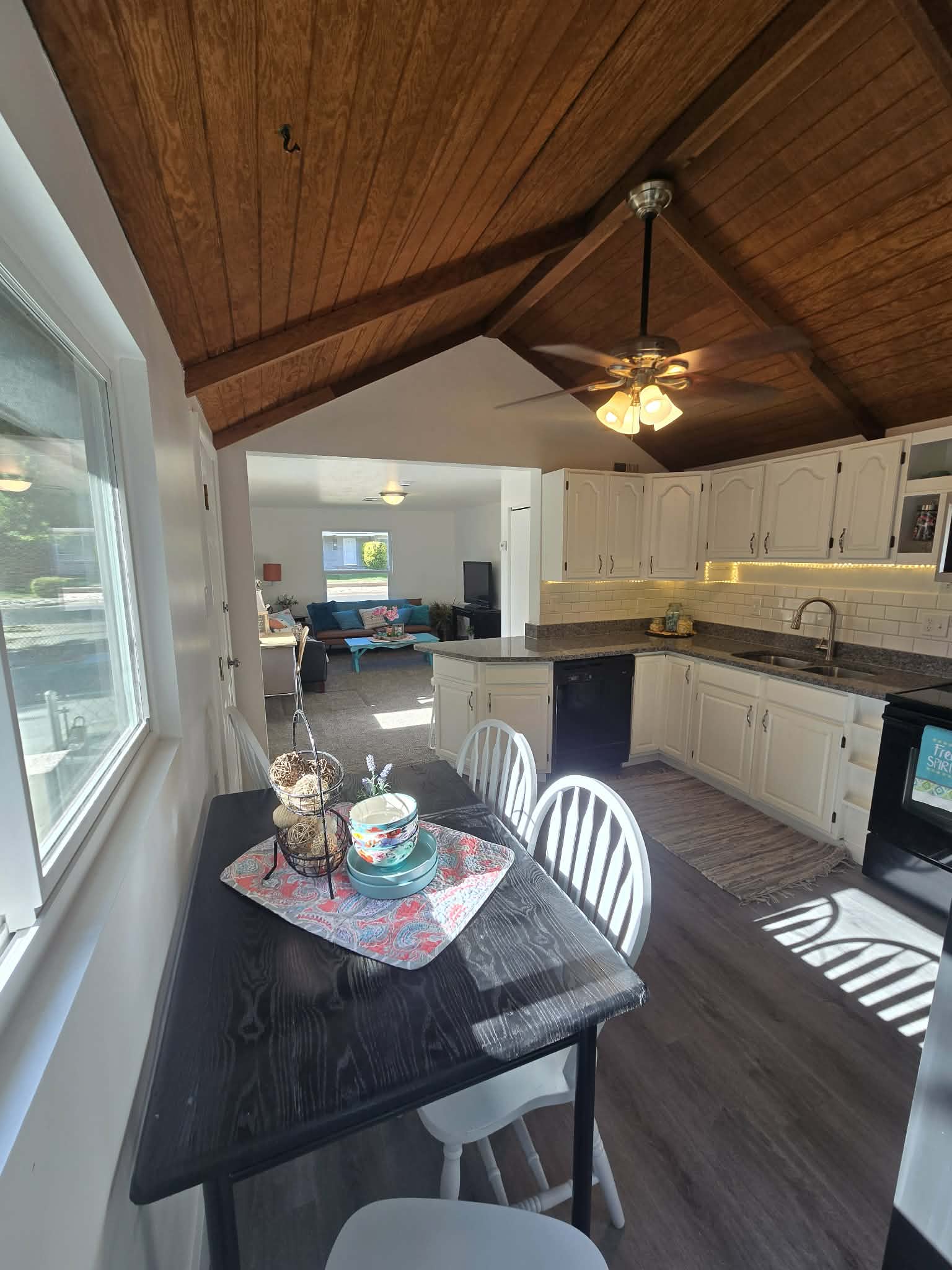 Open-concept kitchen and dining area featuring a vaulted wood-plank ceiling, white cabinetry with under-cabinet lighting, a central kitchen island, and wood-finish flooring