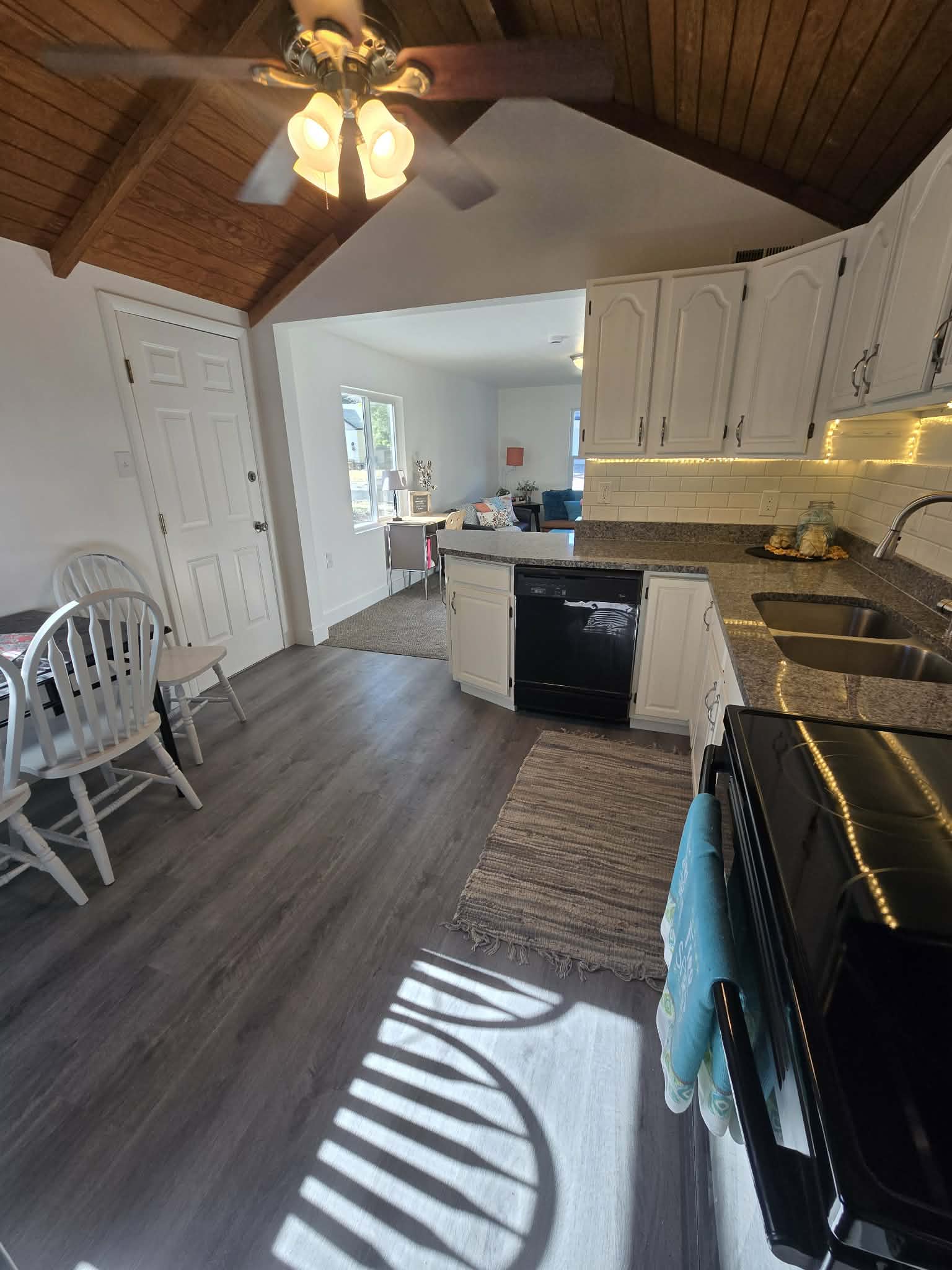 Open-concept kitchen featuring wood-finish flooring, white cabinetry, integrated appliances, and a tiled backsplash