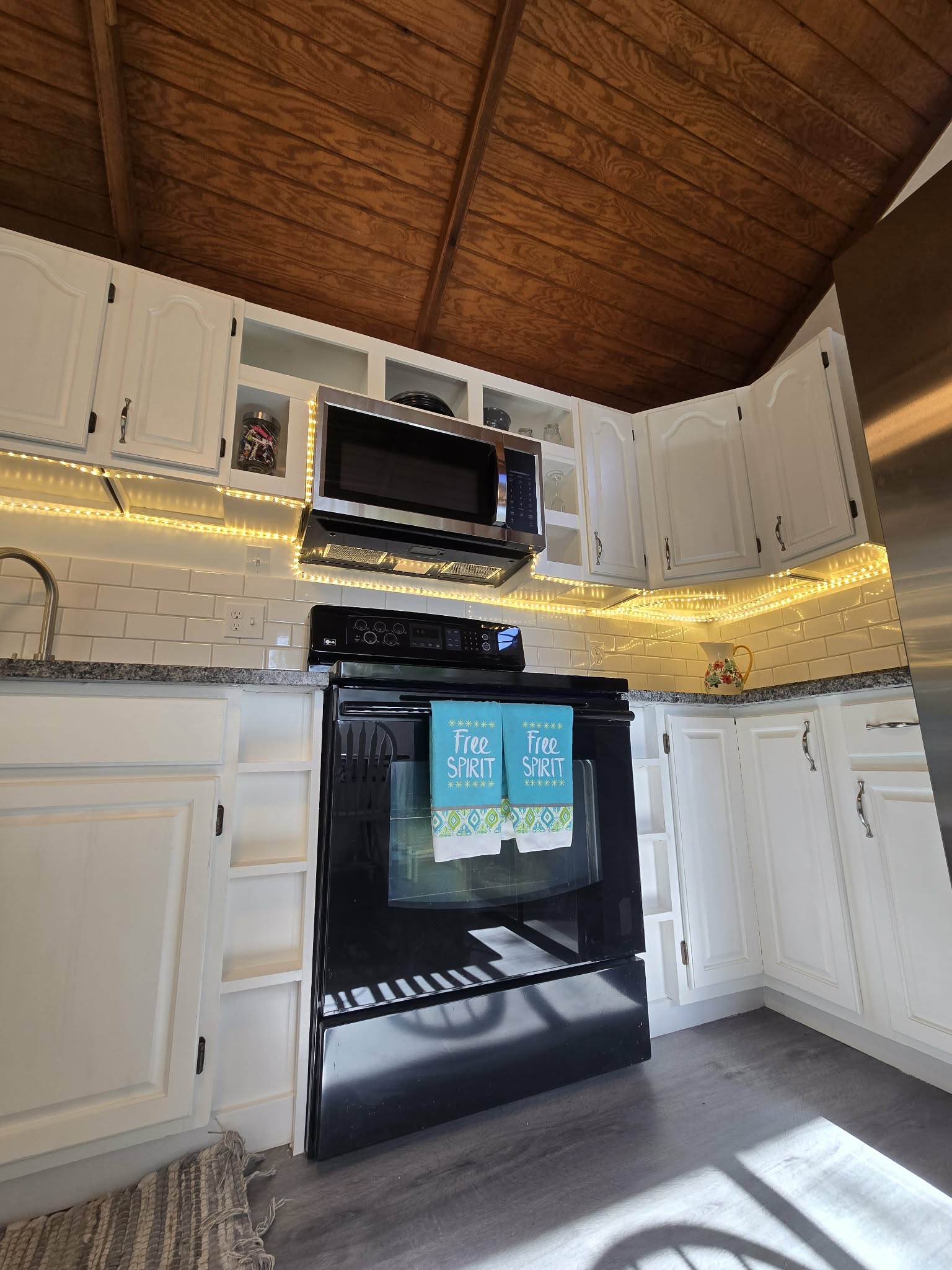 Kitchen featuring a wood-finish vaulted ceiling, white cabinetry with dark hardware, a stainless steel over-the-range microwave, and a black electric range