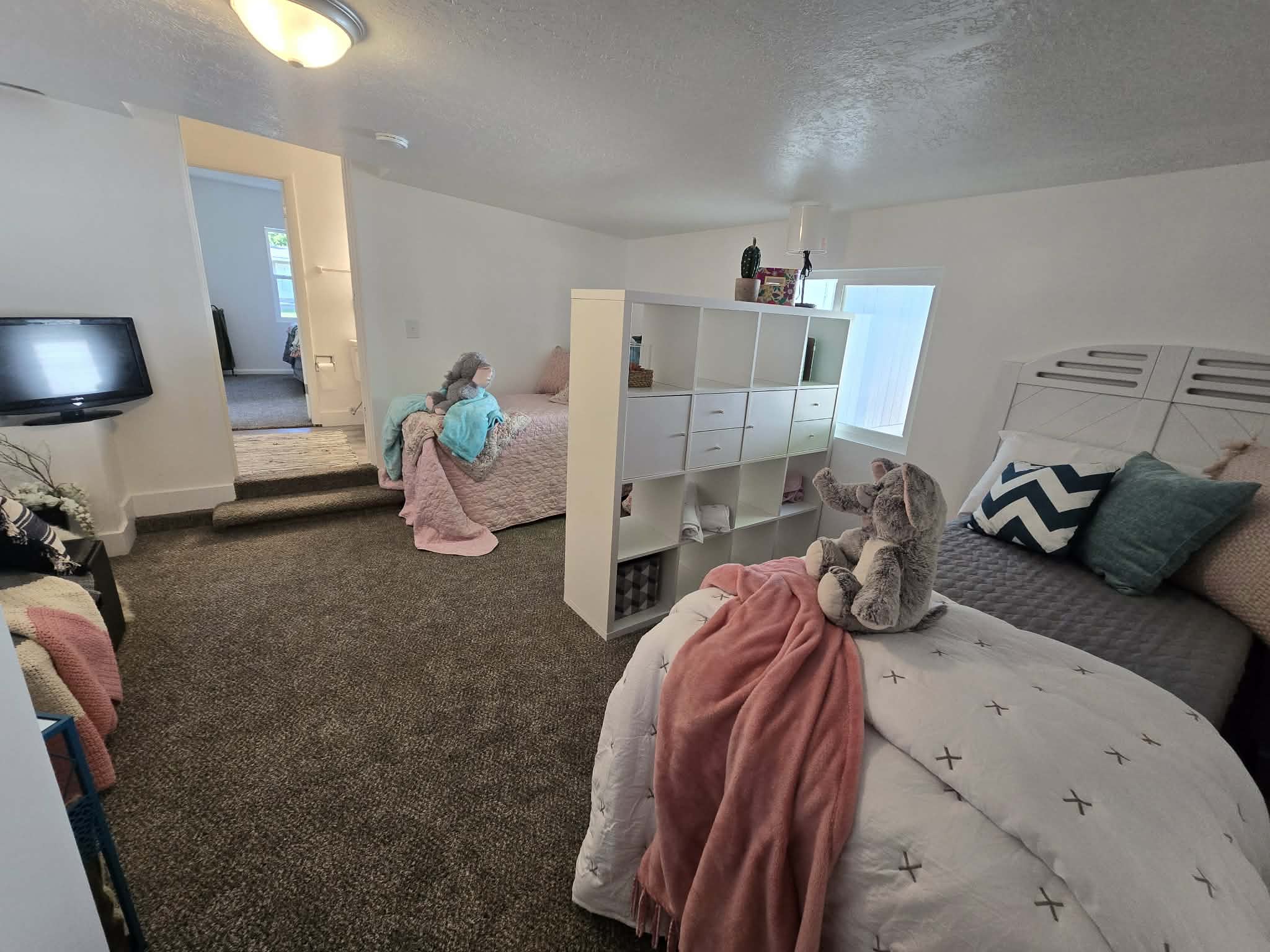 Carpeted room featuring a white painted headboard, integrated shelving unit, and a window providing natural light