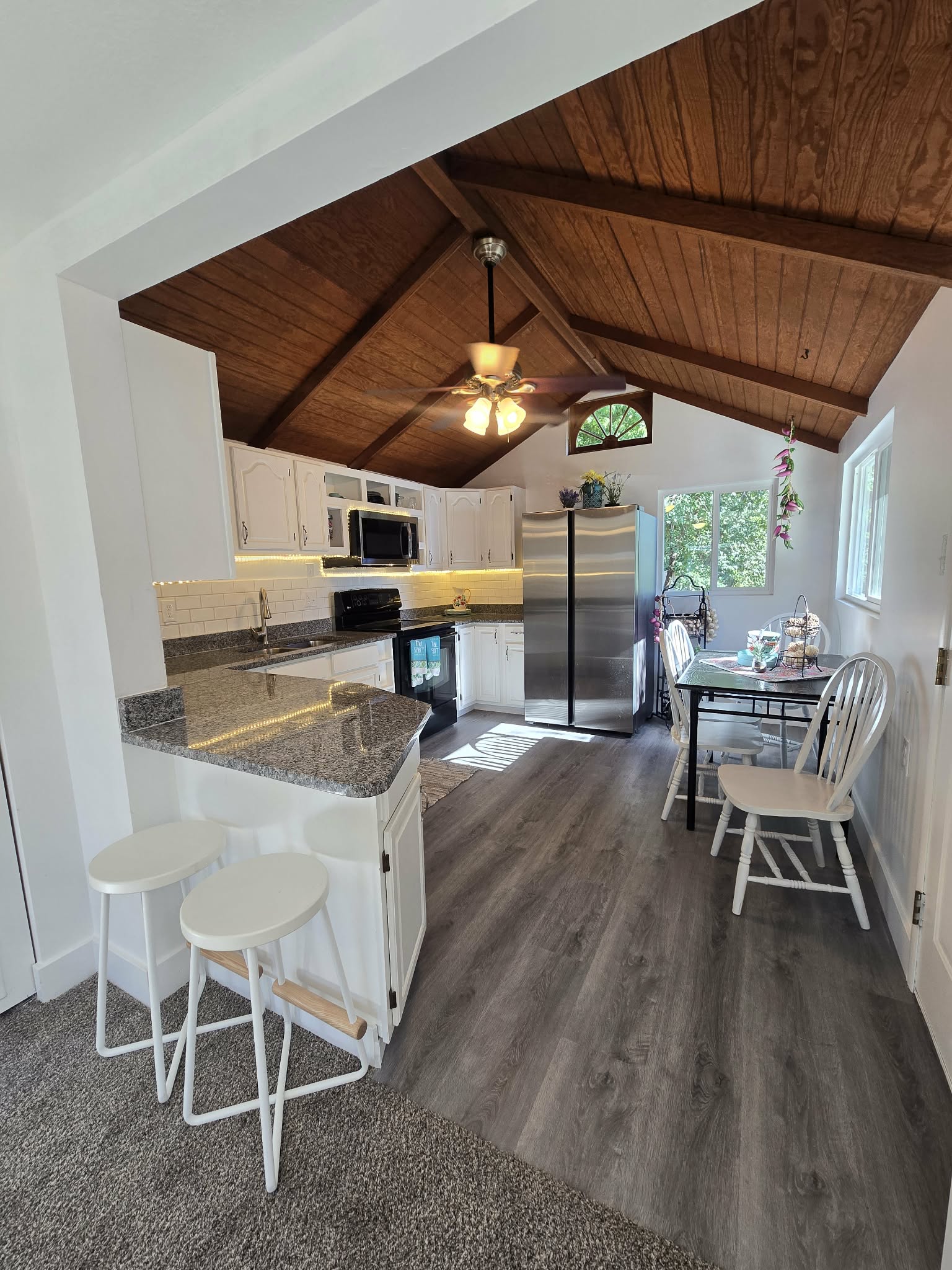 Kitchen featuring a vaulted wood-paneled ceiling with exposed beams, white cabinetry, a breakfast bar with a stone-finish countertop, stainless steel refrigerator, and wood-finish flooring