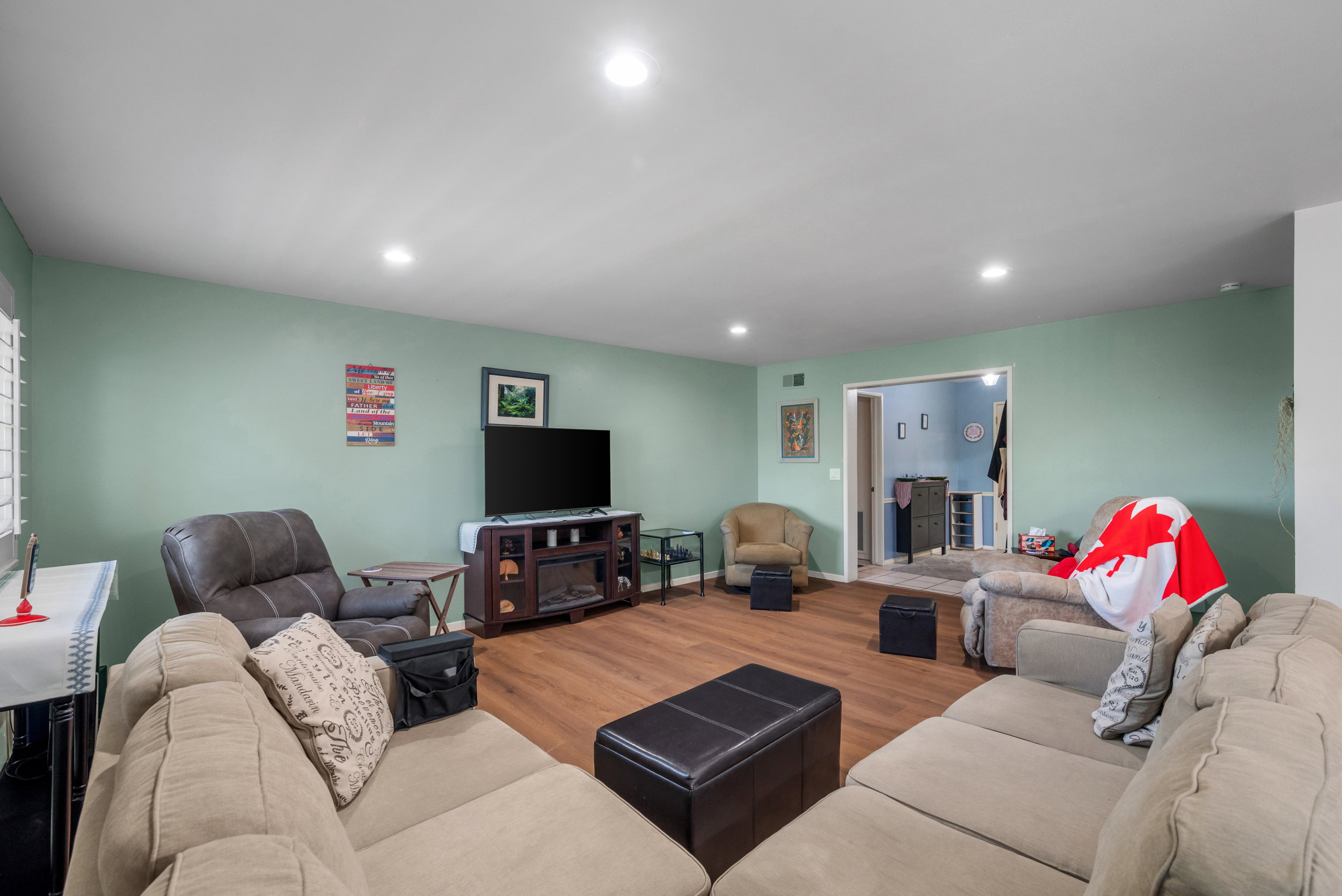 Spacious living area featuring wood-finish flooring, recessed lighting, and a window with plantation shutters