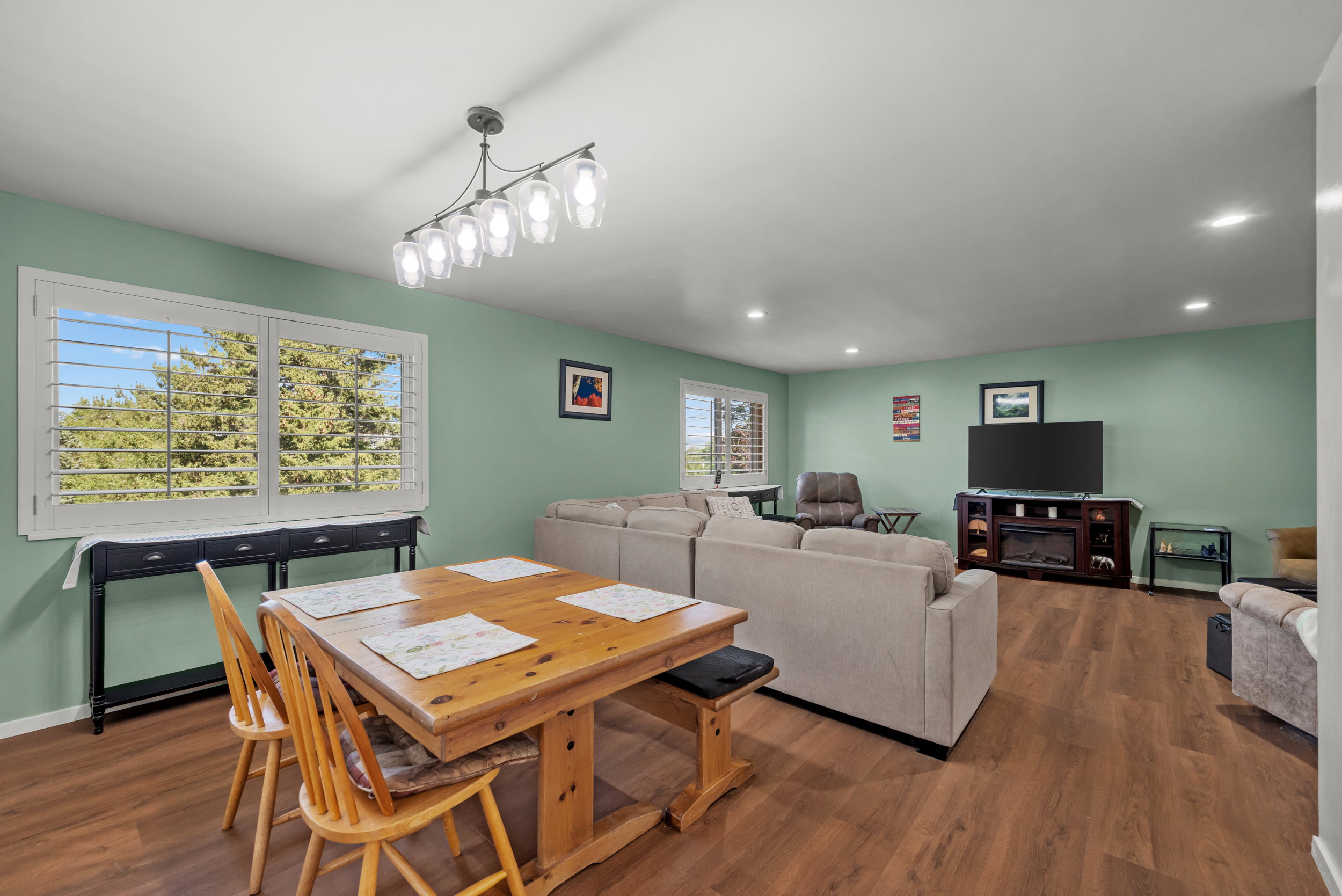 Open-concept living area featuring wood-finish flooring, recessed lighting, and a multi-light linear chandelier