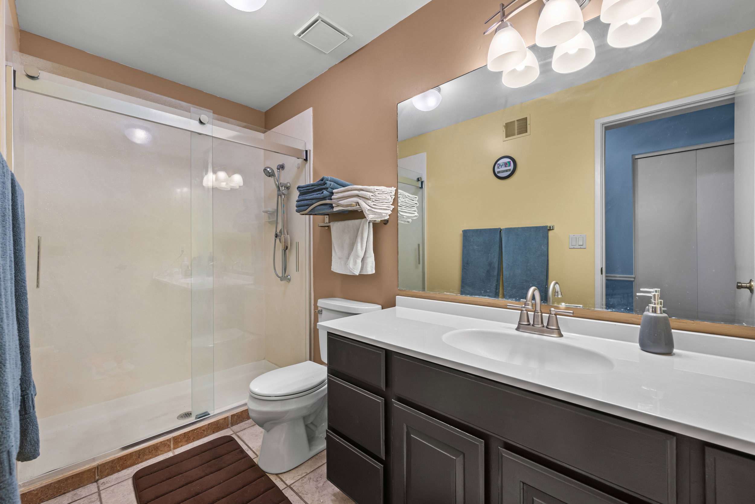 Bathroom featuring a modern vanity with an integrated sink and brushed nickel faucet, a spacious mirror, and a glass-enclosed shower with a handheld showerhead