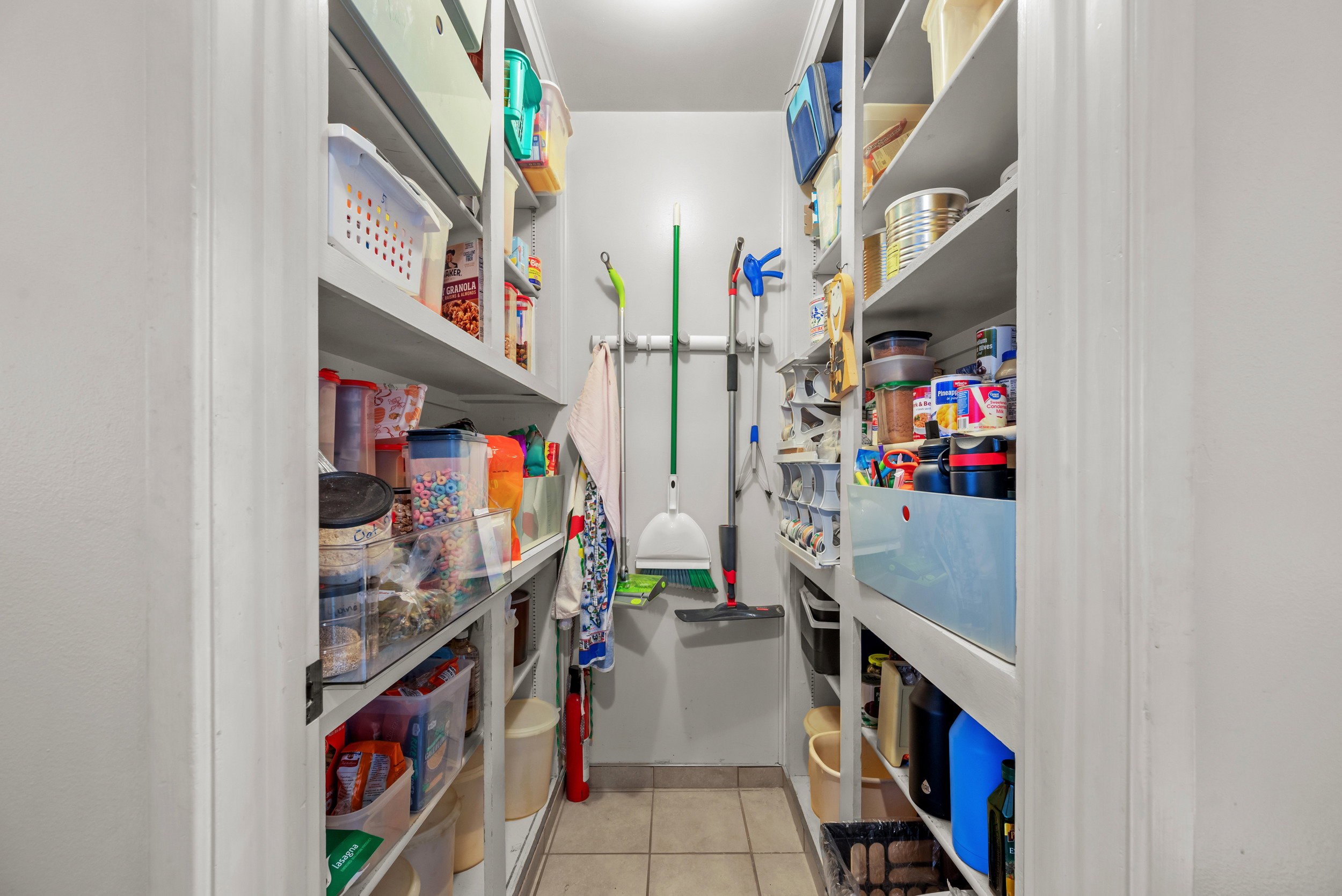 Walk-in pantry featuring extensive built-in shelving, durable tile flooring, and light-toned walls