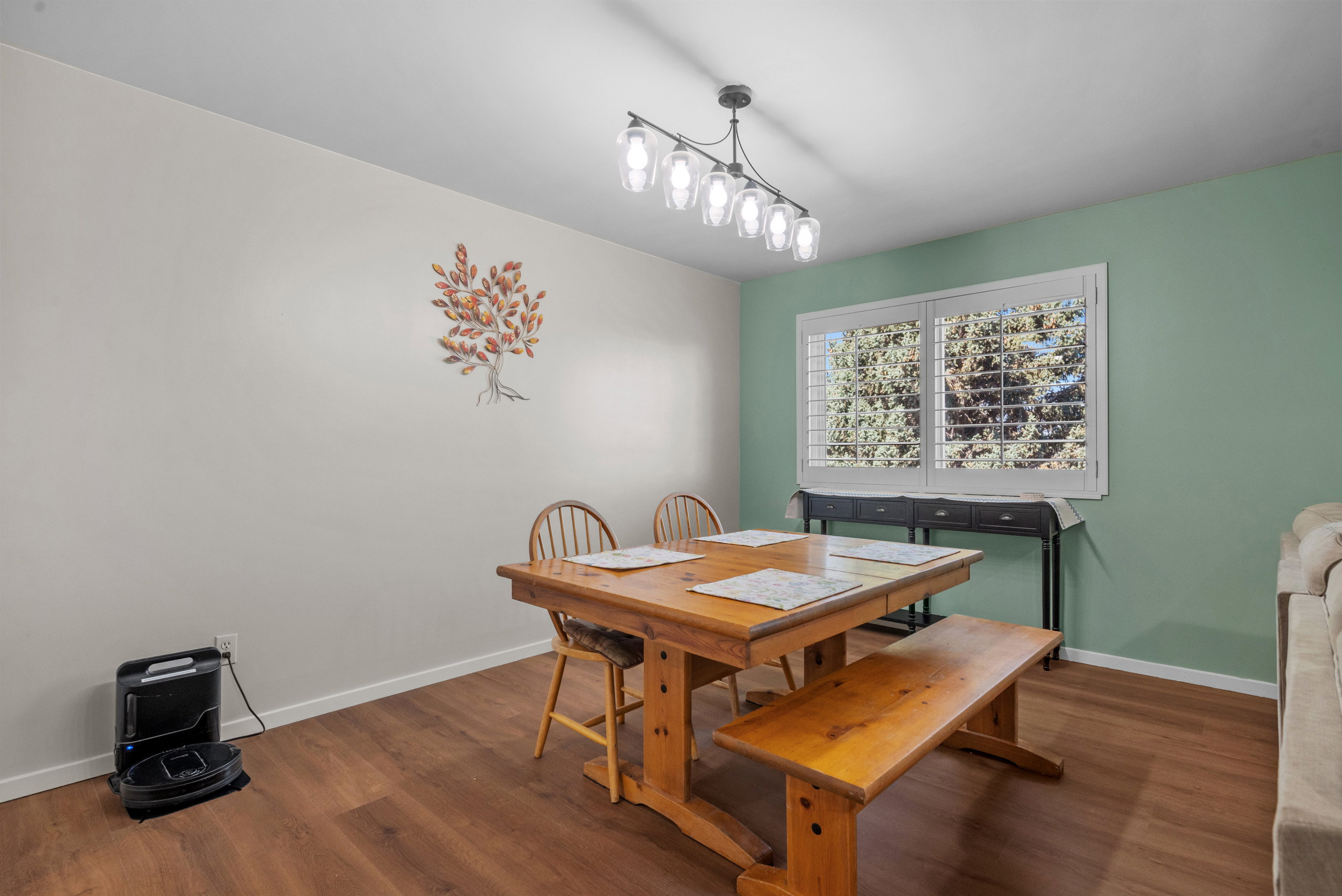 Dining area featuring wood-finish flooring, a contemporary linear chandelier, and a large window with white plantation shutters